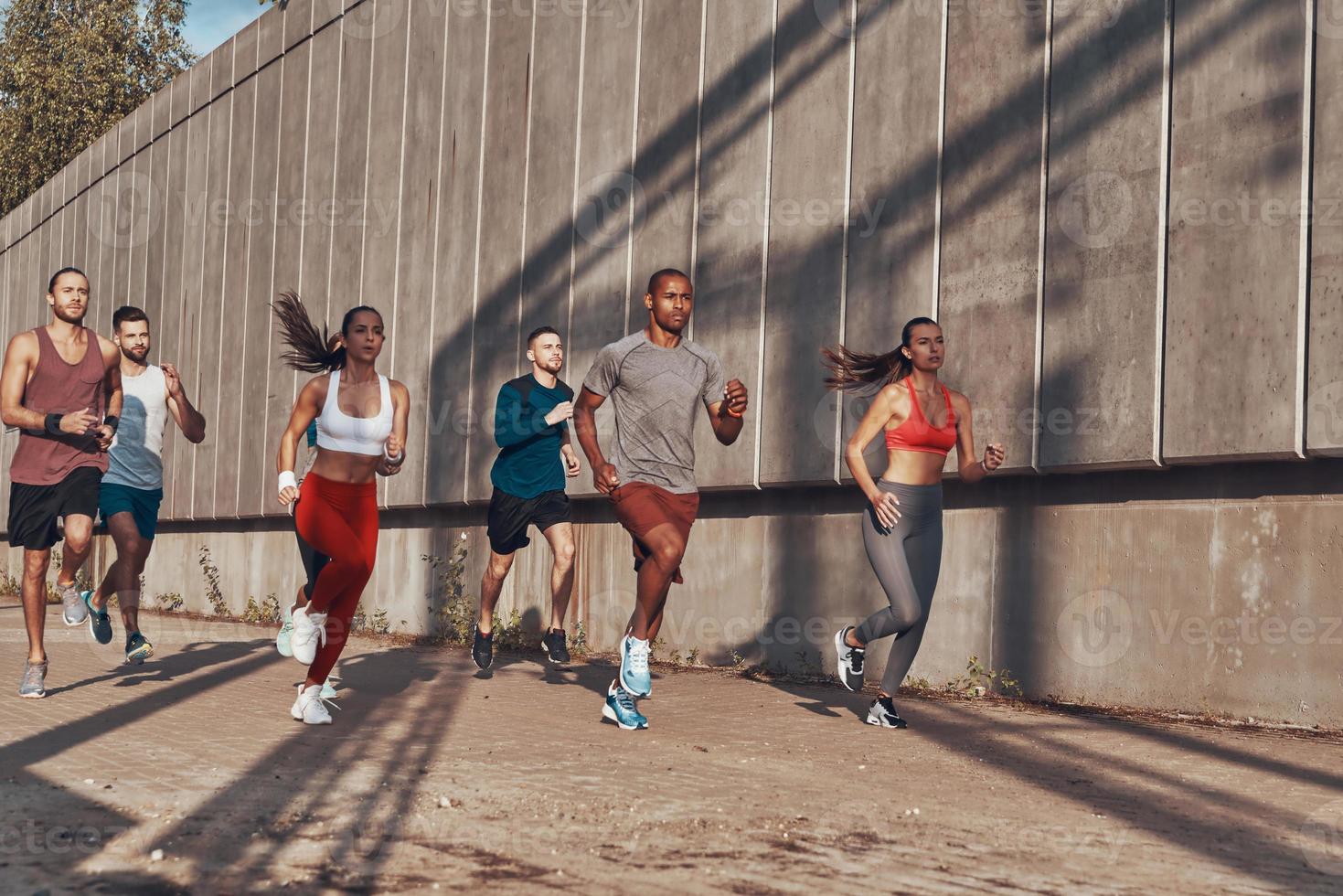 vol lengte van mensen in sport- kleding jogging terwijl oefenen Aan de trottoir buitenshuis foto