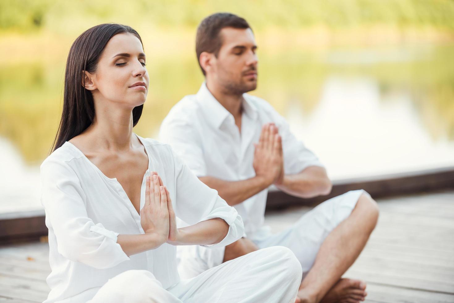 ochtend- meditatie. mooi jong paar in wit kleding mediteren buitenshuis samen en houden ogen Gesloten foto