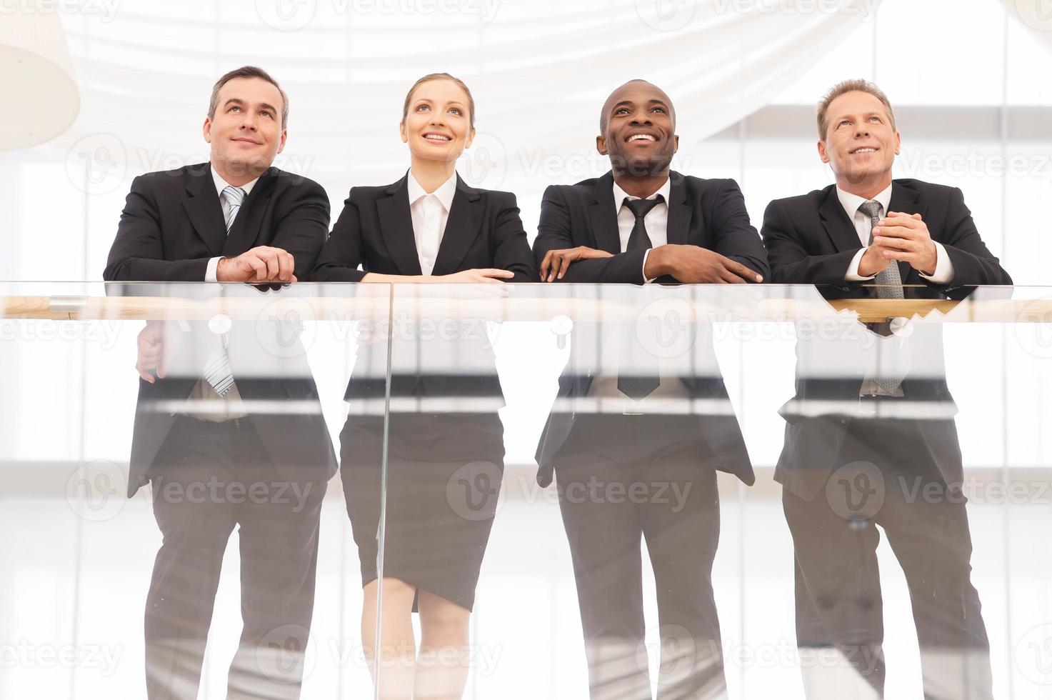 bedrijf team. laag hoek visie van vier zelfverzekerd bedrijf mensen staand dichtbij naar elk andere en glimlachen foto