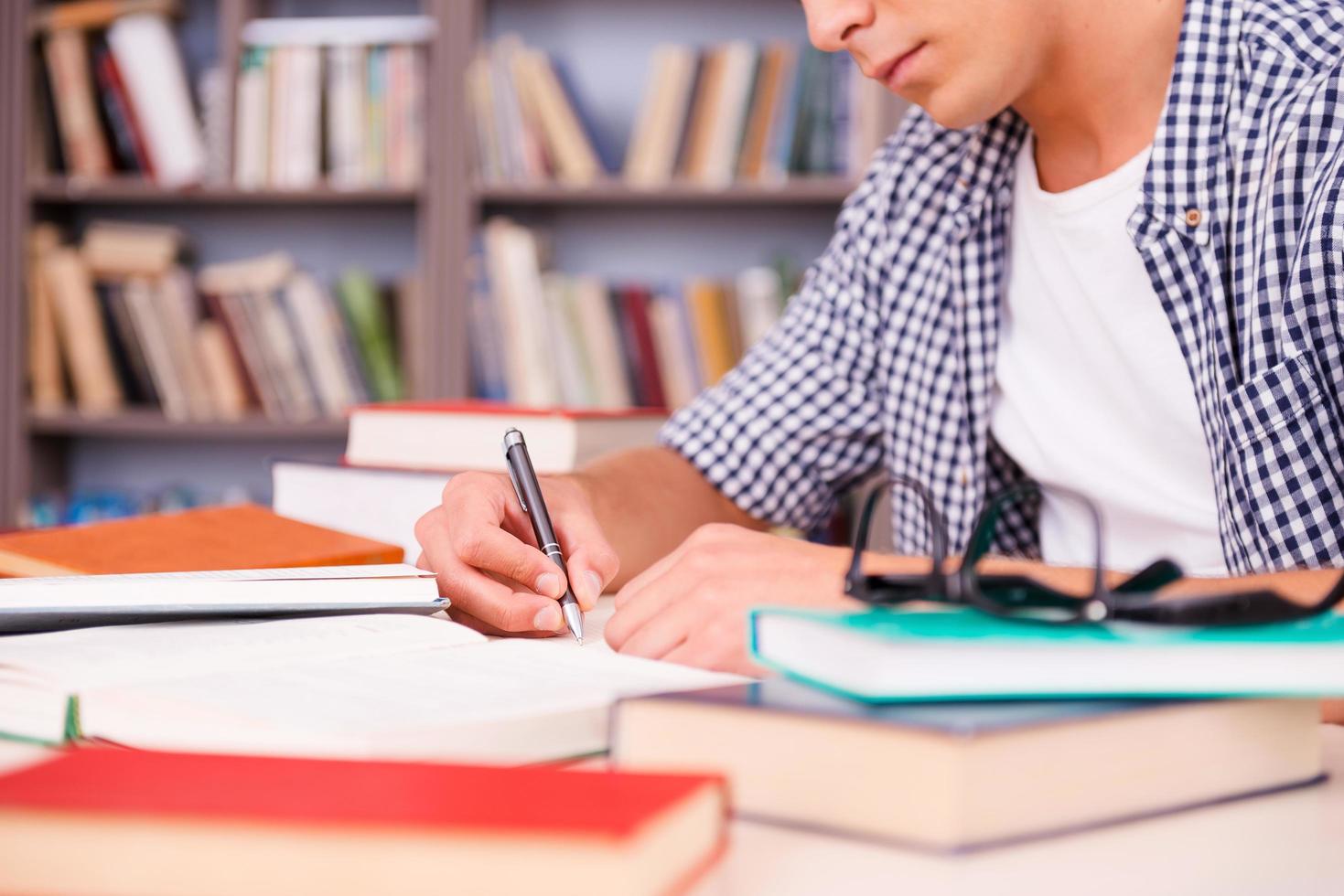 zelfverzekerd leerling aan het studeren. kant visie van zelfverzekerd jong Mens maken Onderzoek terwijl zittend Bij de bureau in bibliotheek foto