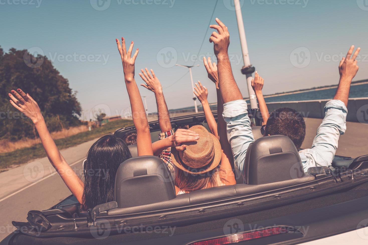 genieten van weg reis. achterzijde visie van jong gelukkig mensen genieten van weg reis in hun converteerbaar en verhogen hun armen omhoog foto