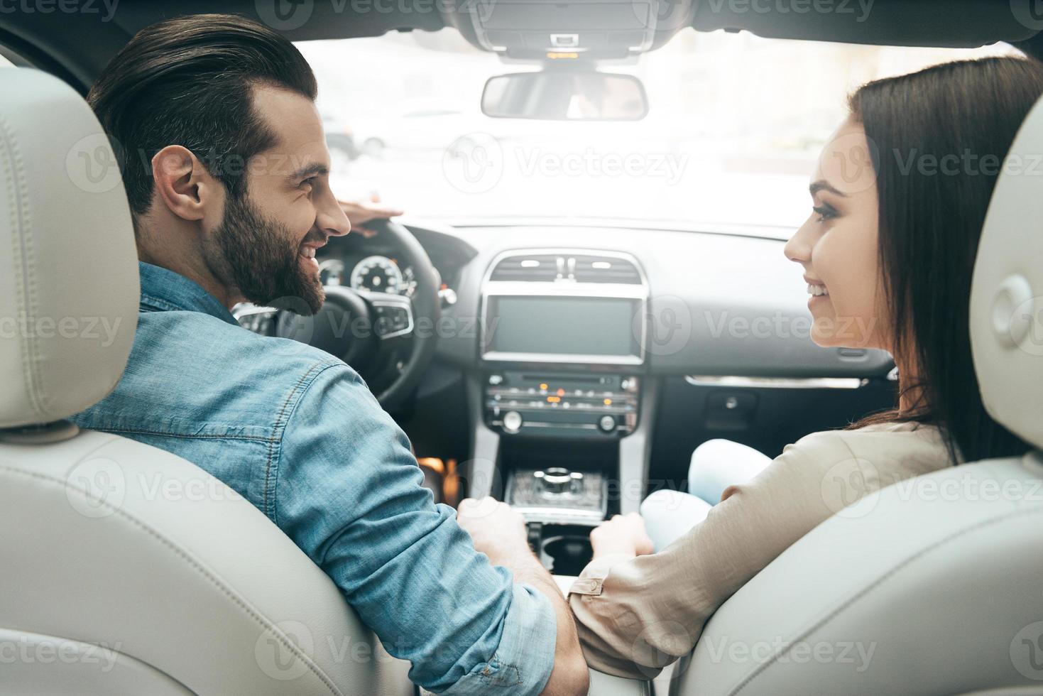 genieten van de moment. achterzijde visie van jong paar zittend Aan de voorkant passagier stoelen en op zoek Bij elk andere terwijl knap Mens het rijden een auto foto