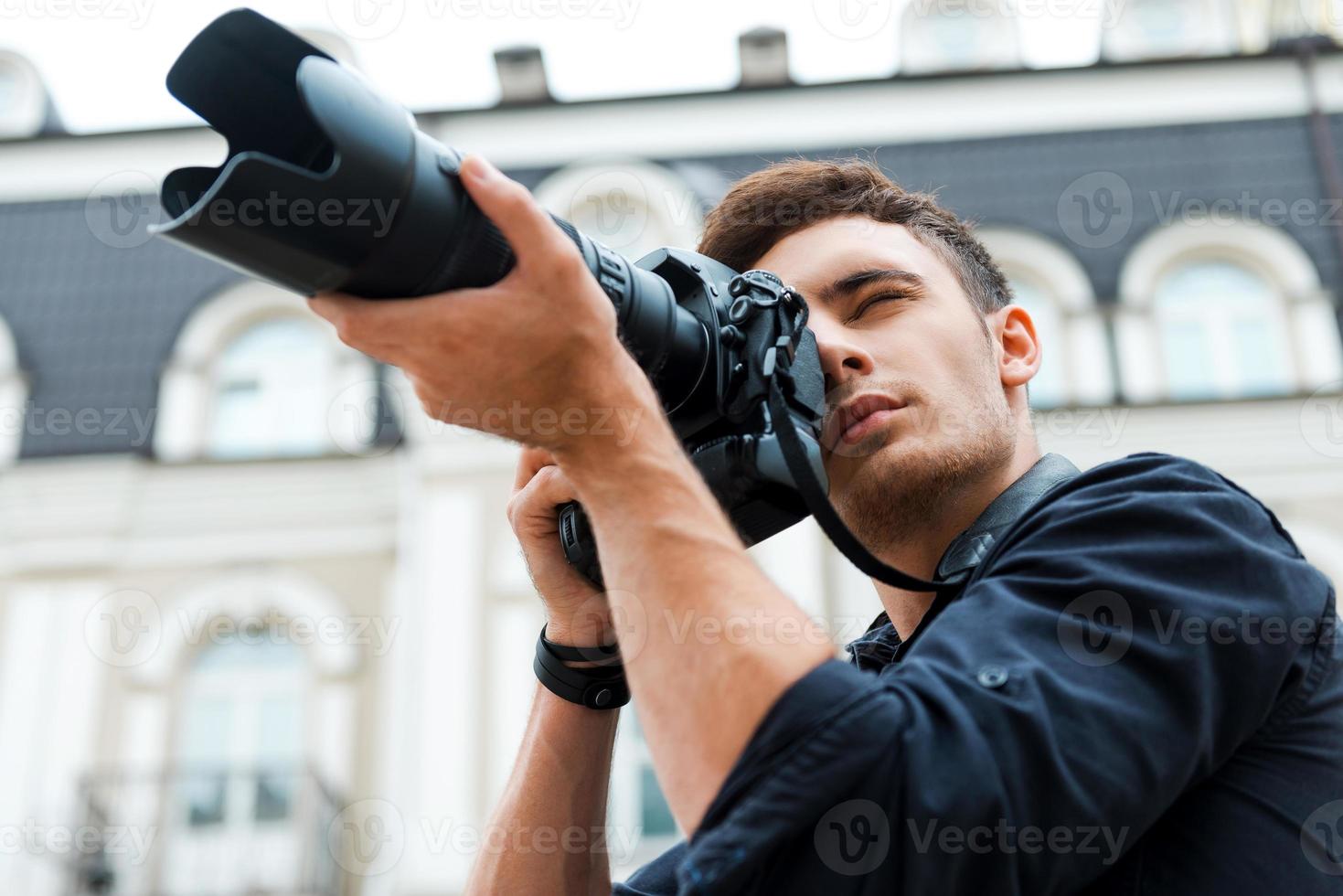 nemen een perfect schot. laag hoek visie van jong Mens fotograferen iets terwijl staand buitenshuis foto