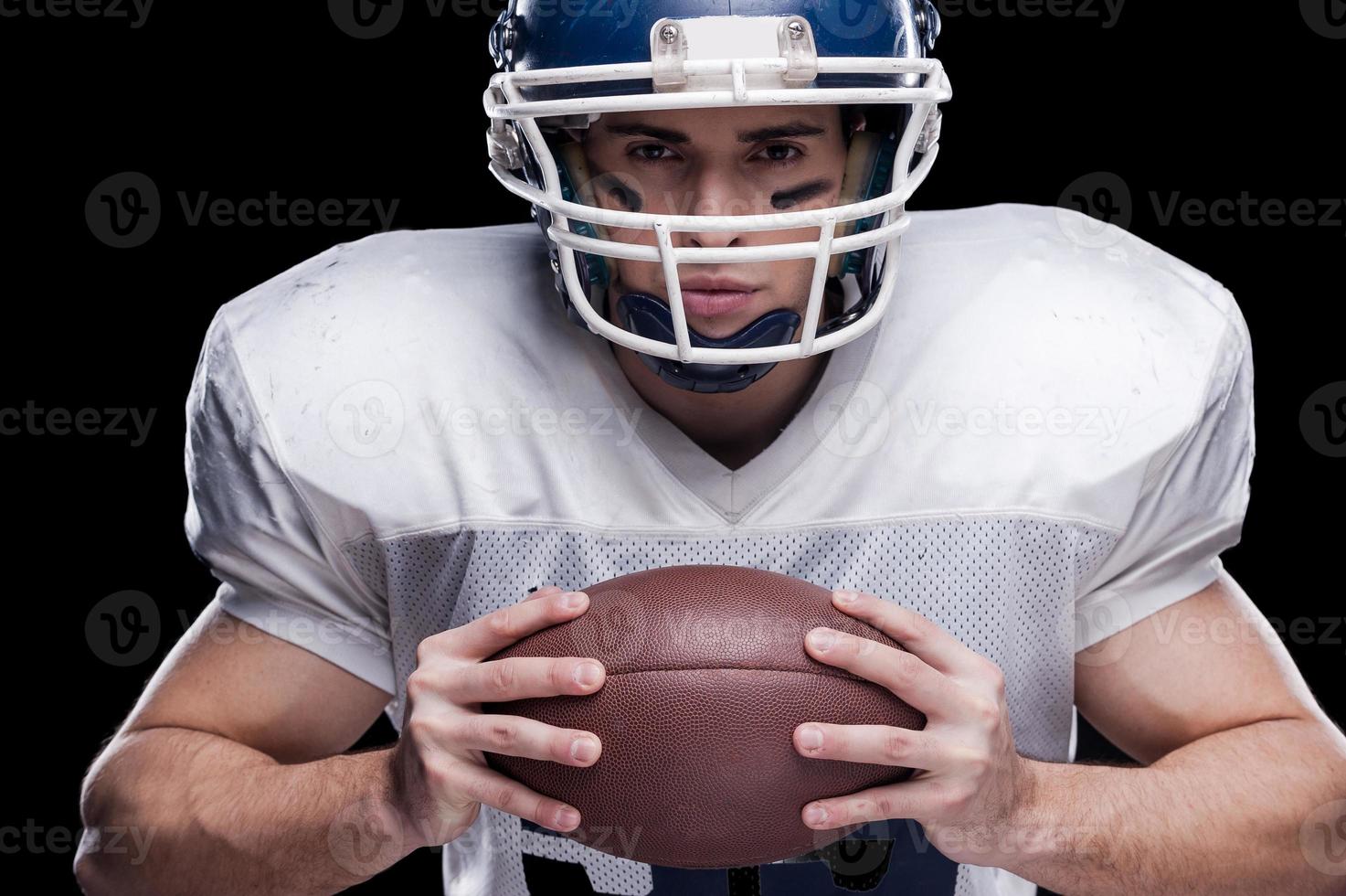 Amerikaans voetbal is mijn leven Amerikaans Amerikaans voetbal speler op zoek Bij camera en Holding bal terwijl staand tegen zwart achtergrond foto