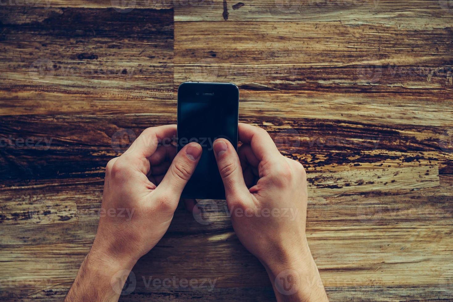 typen snel bericht. detailopname top visie van mannetje handen Holding mobiel telefoon over- de rustiek houten bureau foto