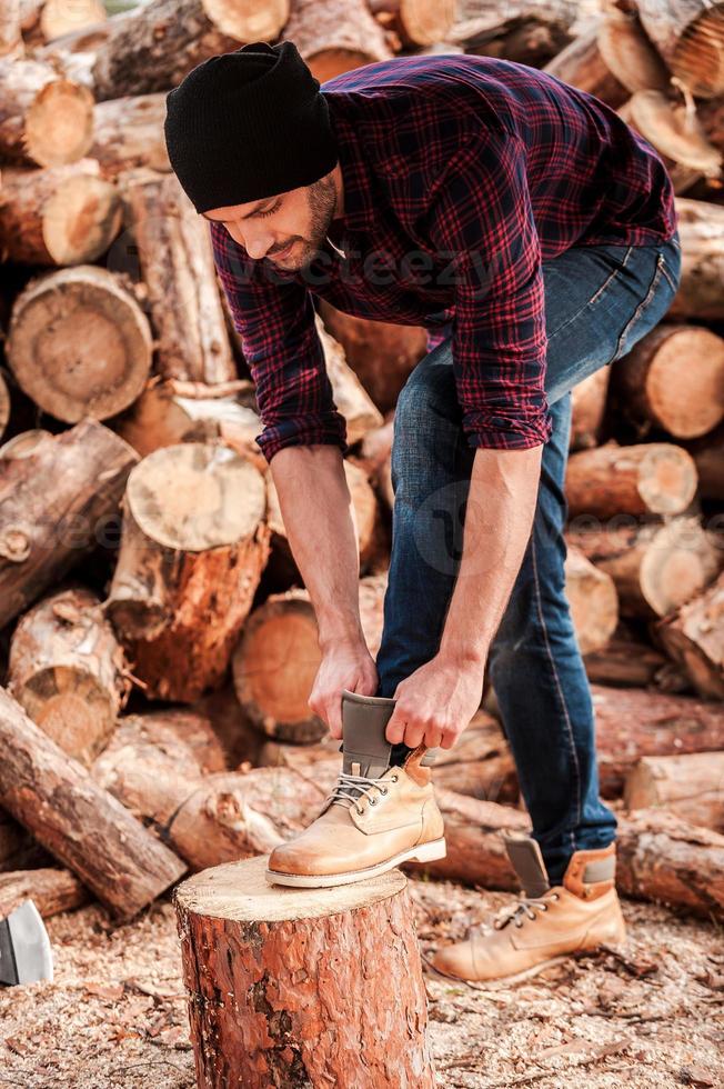 krijgen klaar naar werk. vol lengte van zelfverzekerd jong boswachter aanpassen zijn schoenen terwijl leunend Bij de log foto