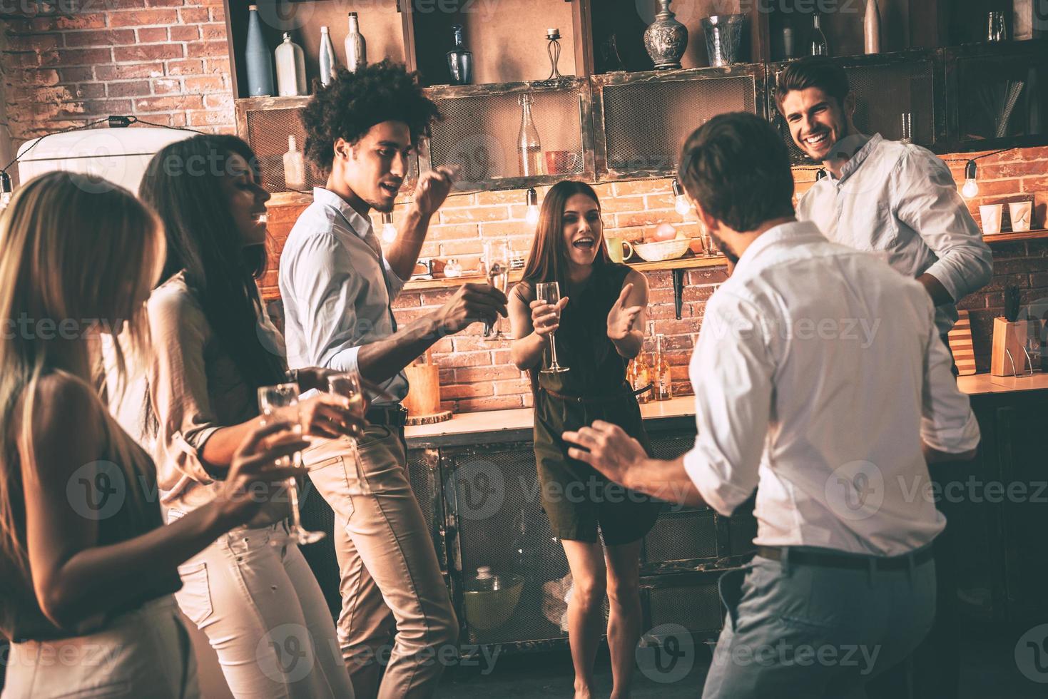 partij dat nooit loopt af. vrolijk jong mensen dansen en drinken terwijl genieten van huis partij Aan de keuken foto