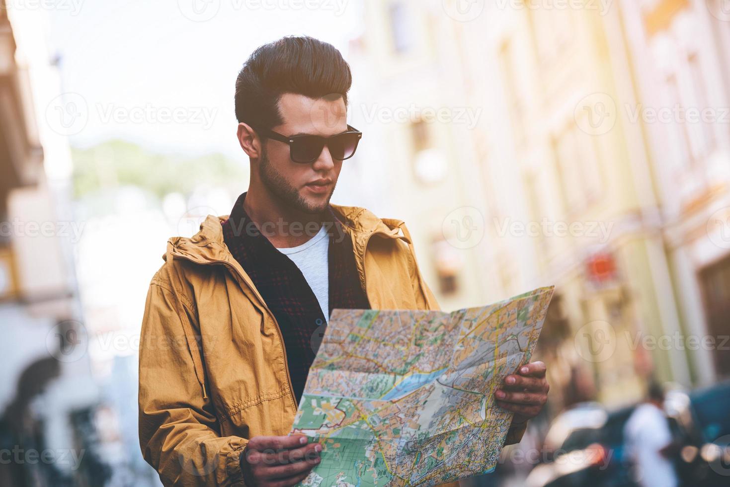 Mens onderzoeken kaart. knap jong Mens Holding kaart en op zoek Bij het terwijl staand Aan de stad straat foto