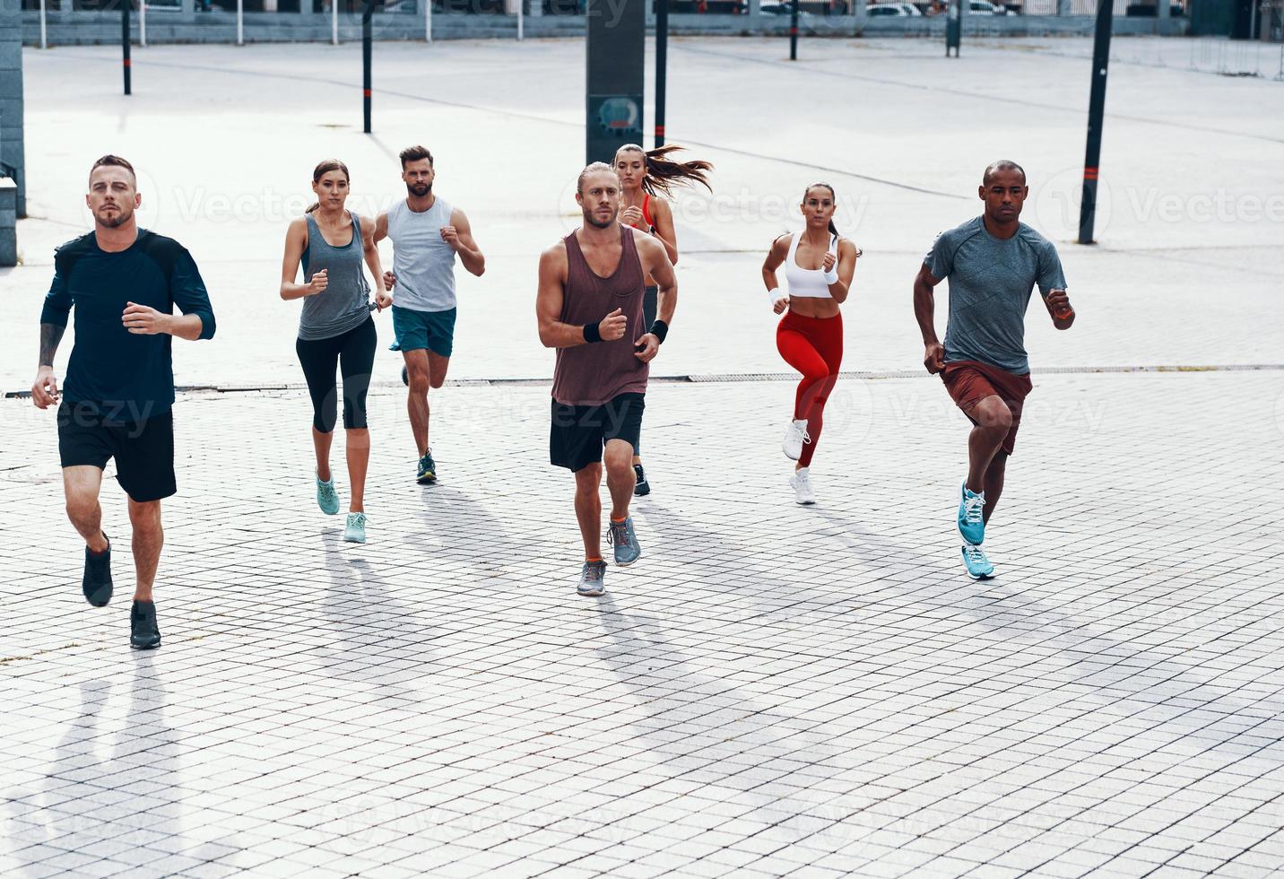 vol lengte van mensen in sport- kleding jogging terwijl oefenen Aan de trottoir buitenshuis foto