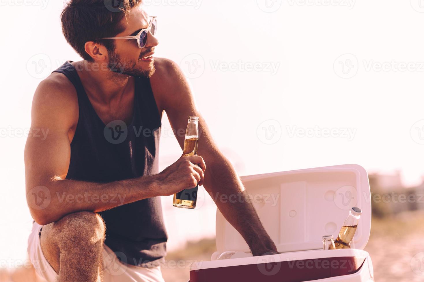 bier tijd. knap jong Mens nemen bier flessen van koeler terwijl ontspannende Aan de strand foto