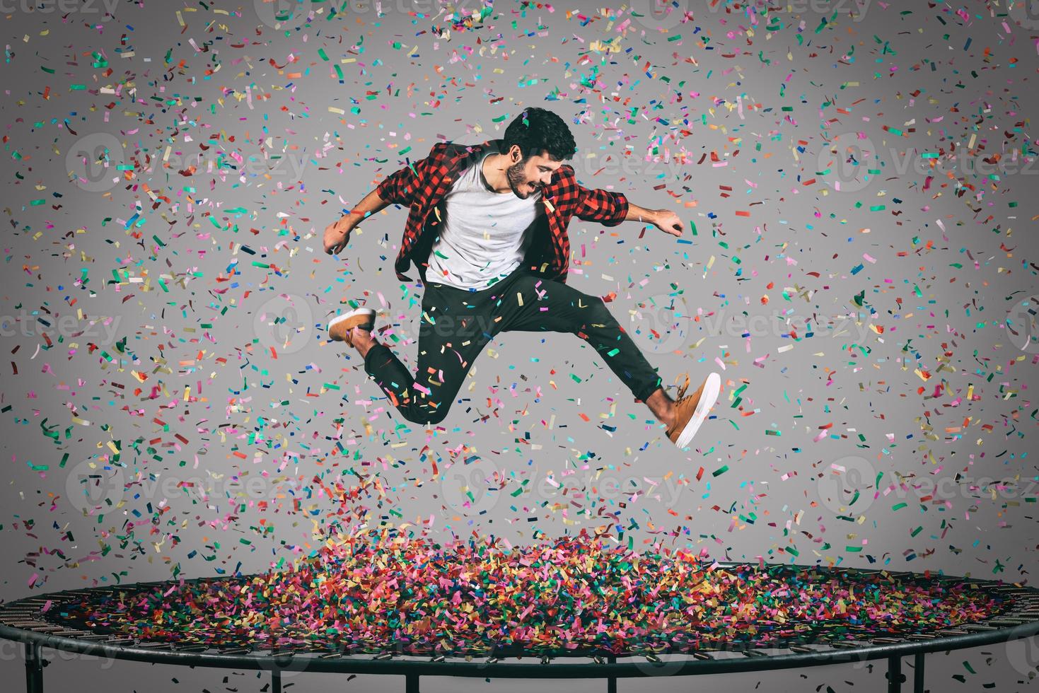 leven een helder leven. in de lucht schot van knap jong Mens jumping Aan trampoline met confetti allemaal in de omgeving van hem foto