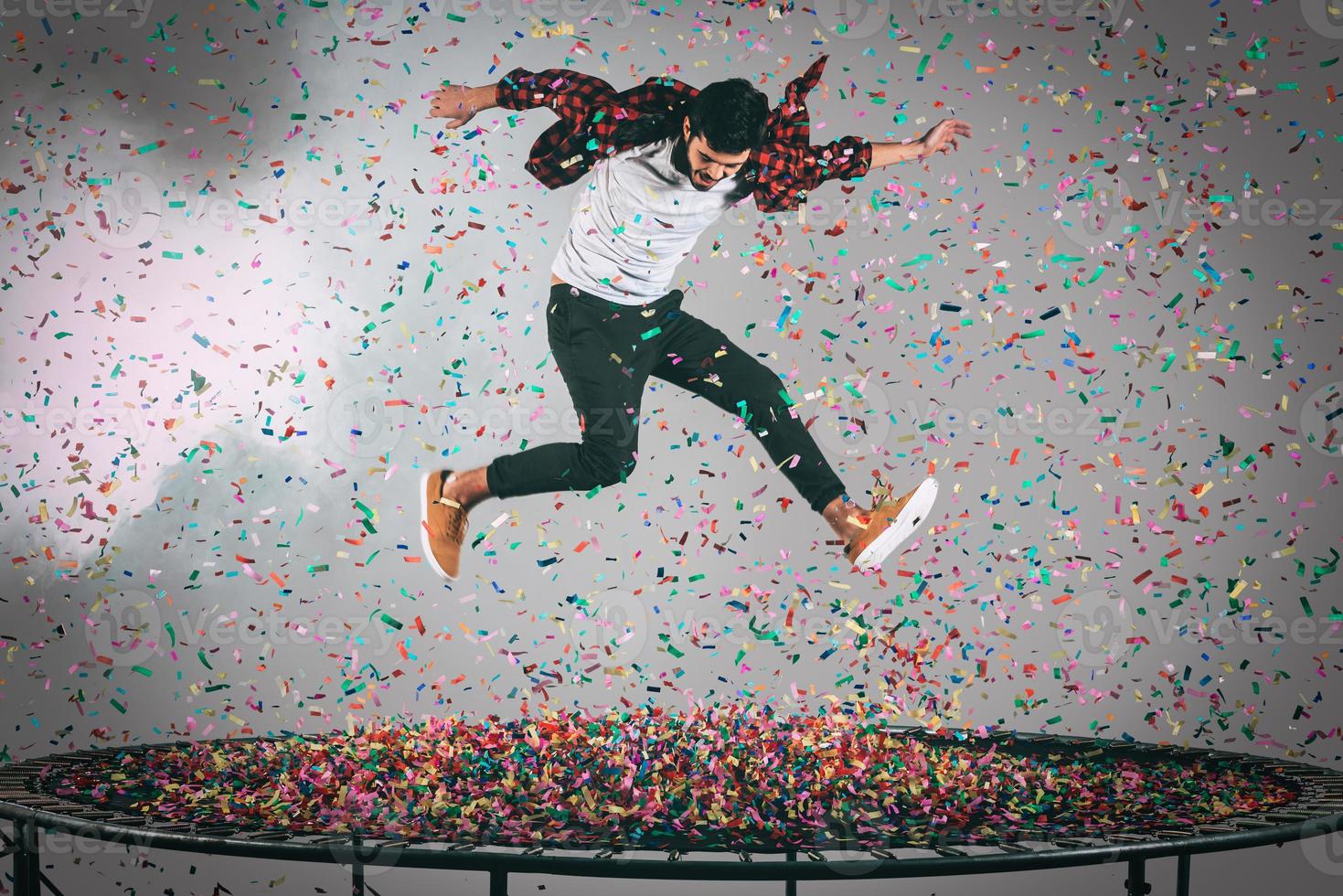 kleurrijk plezier. in de lucht schot van knap jong Mens jumping Aan trampoline met confetti allemaal in de omgeving van hem foto