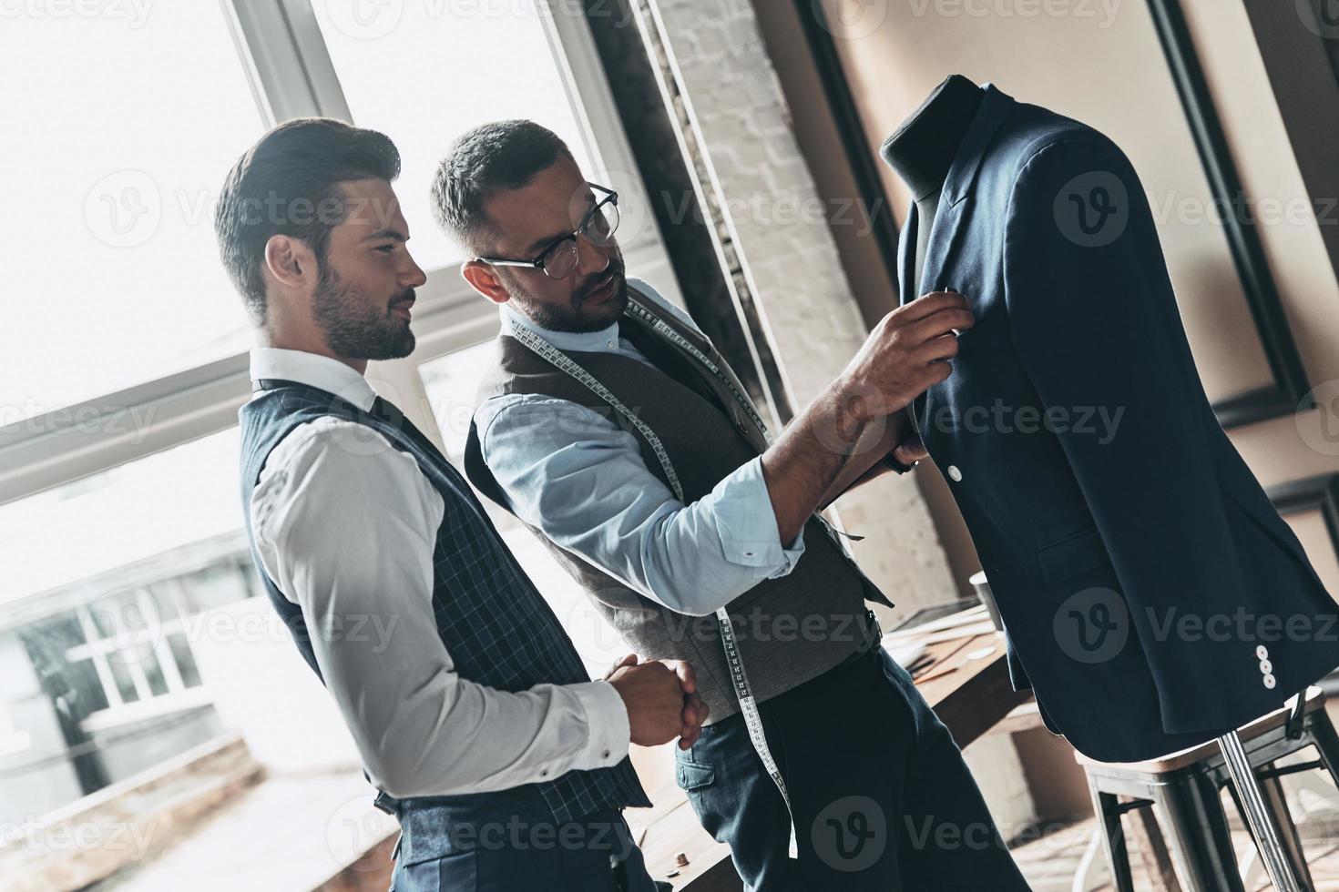 zijn ontwerpen zijn in vraag naar. twee jong modieus mannen op zoek Bij jasje terwijl staand in werkplaats foto