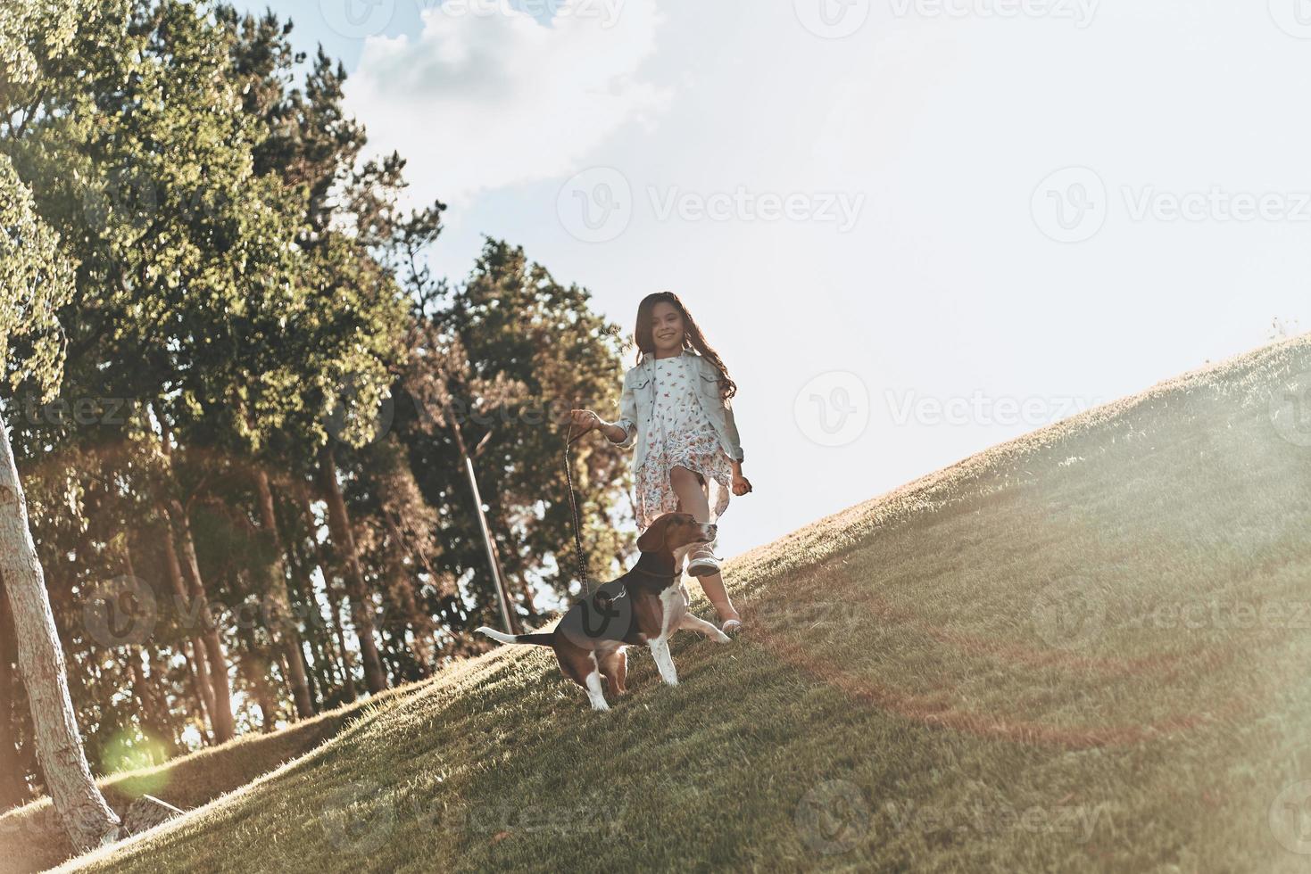 genieten van zomer dag. vol lengte van schattig weinig meisje spelen met haar hond terwijl rennen buitenshuis foto