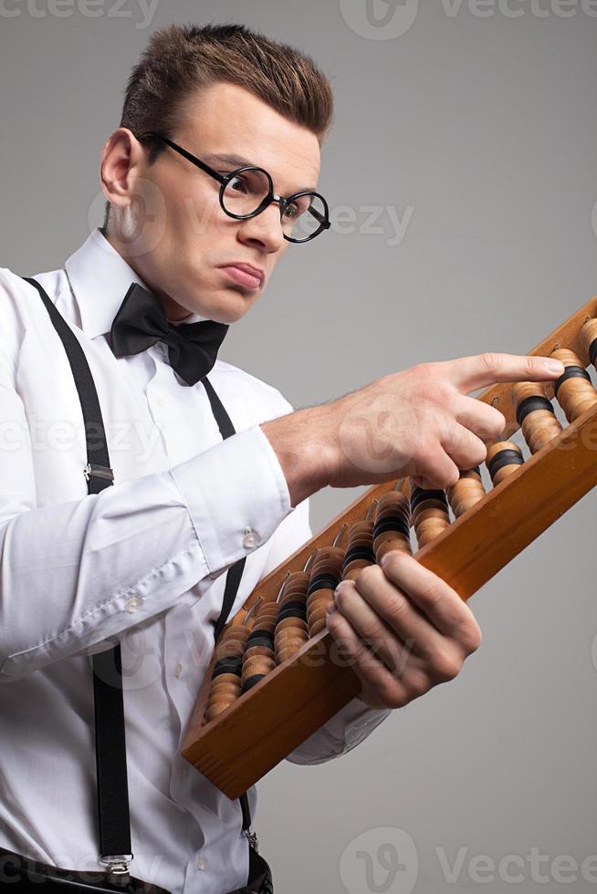 nerd met telraam. laag hoek visie van echt jong Mens in boog stropdas en bretels gebruik makend van telraam terwijl staand tegen grijs achtergrond foto