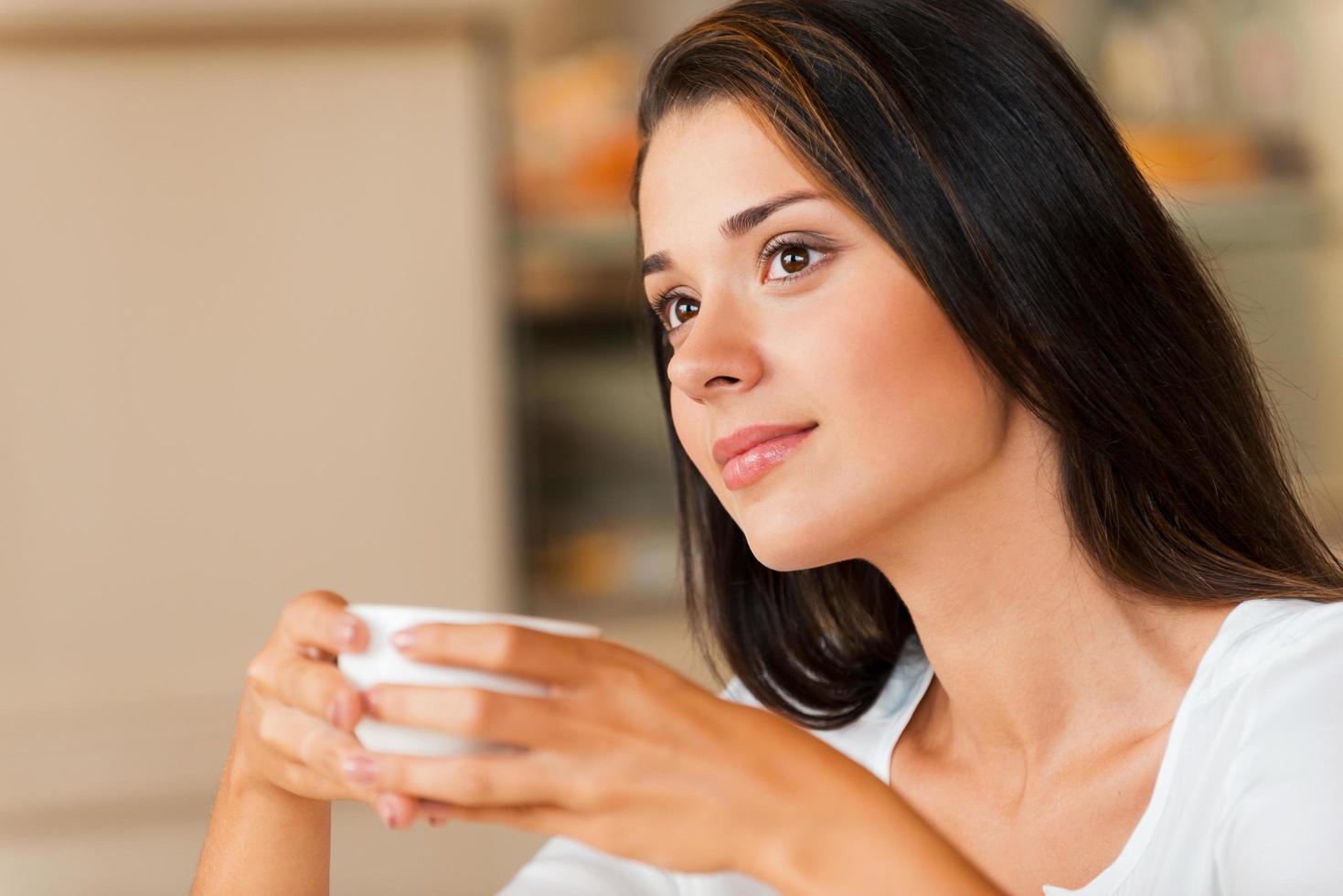 verloren in gedachten. attent jong vrouw Holding koffie kop en op zoek weg terwijl zittend in koffie winkel foto