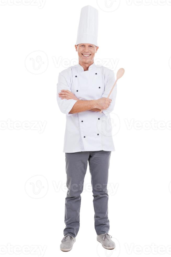 zelfverzekerd chef. vol lengte van zelfverzekerd volwassen chef in wit uniform houden armen gekruiste en glimlachen terwijl staand tegen wit achtergrond foto