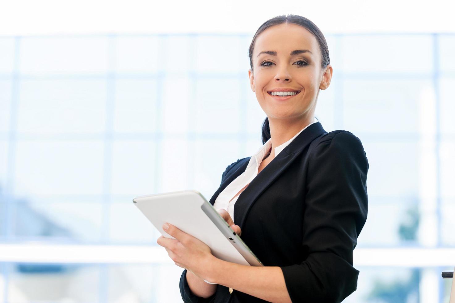 nemen voordelen van digitaal leeftijd. mooi jong vrouw in formele kleding Holding digitaal tablet en glimlachen terwijl staand buitenshuis foto