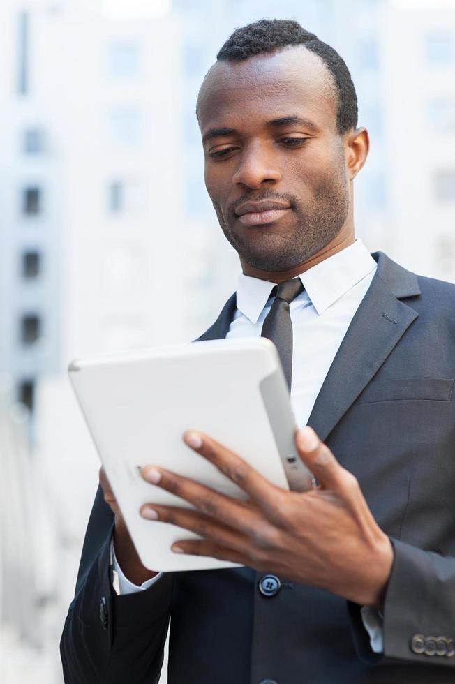 zakenman met digitaal tablet. zelfverzekerd jong Afrikaanse Mens in formele kleding werken Aan digitaal tablet en terwijl staand buitenshuis foto