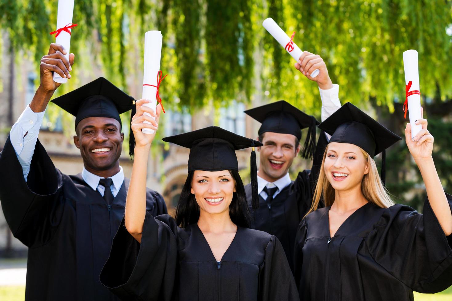 gelukkig afgestudeerden. vier college afgestudeerden tonen hun diploma's en glimlachen terwijl staand dichtbij naar elk andere en foto