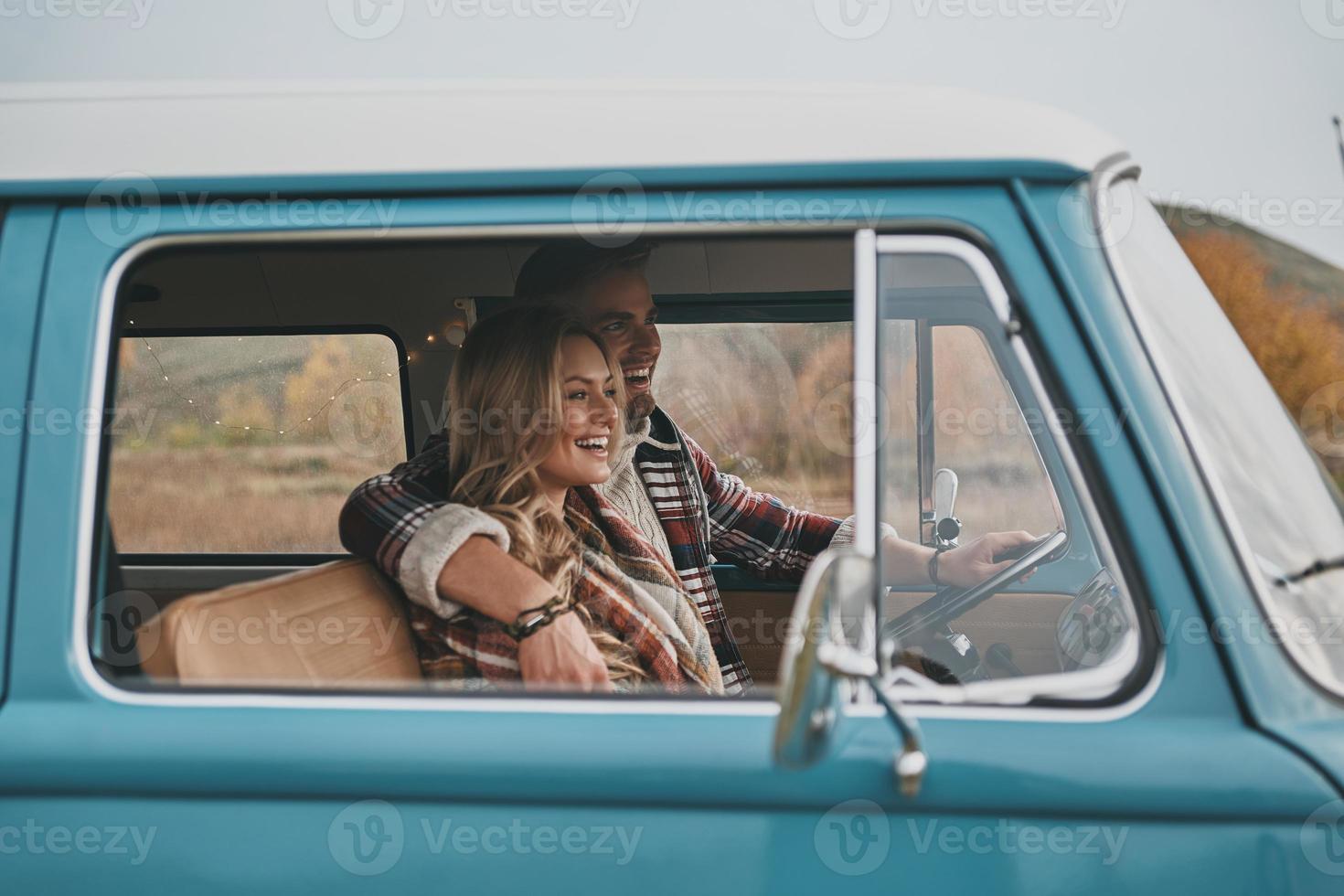 genieten van hun weg reis. mooi jong paar omarmen en glimlachen terwijl zittend in blauw retro stijl mini busje foto