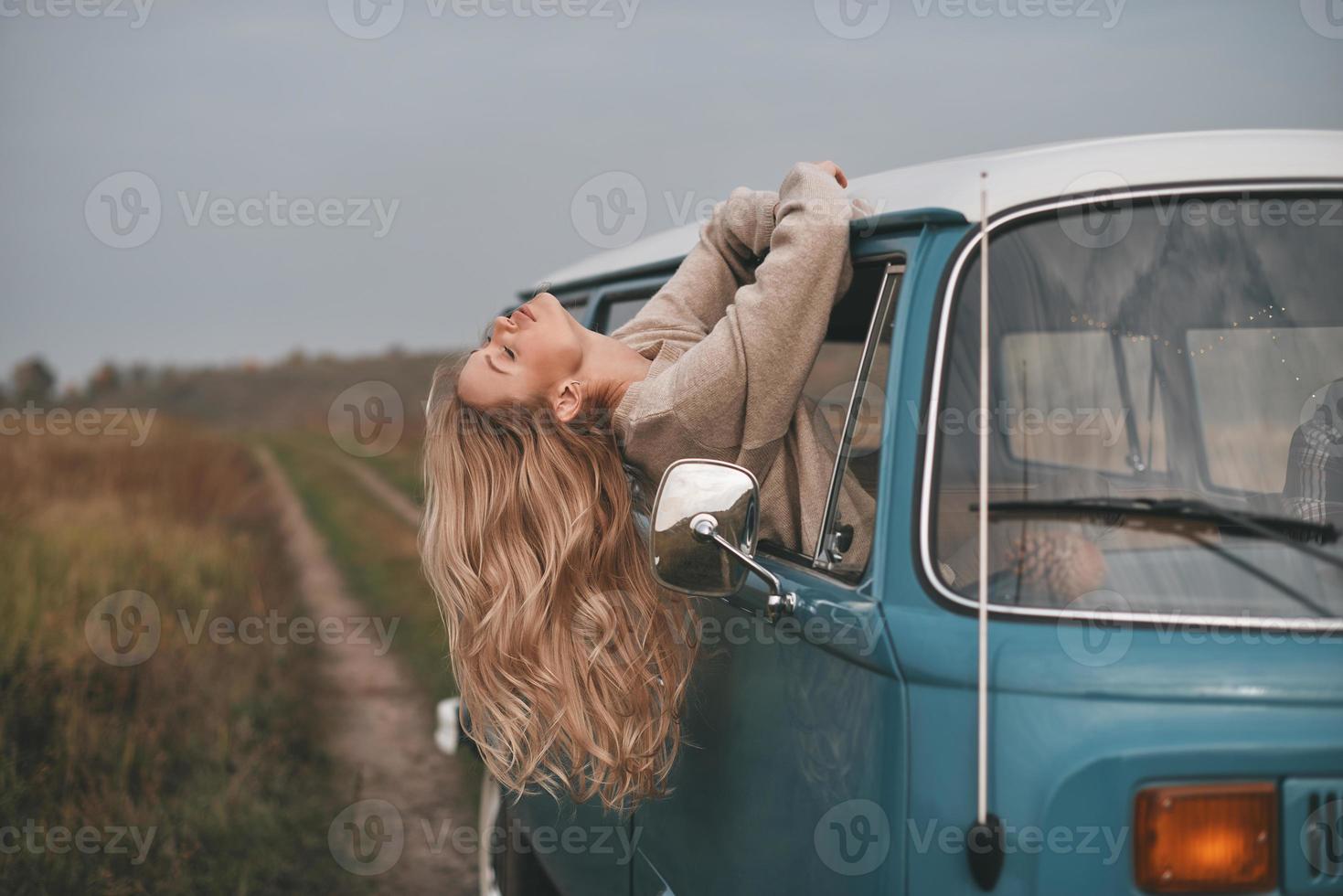 totaal vrij. aantrekkelijk jong vrouw leunend uit de bestelwagens venster terwijl genieten van de auto reizen foto