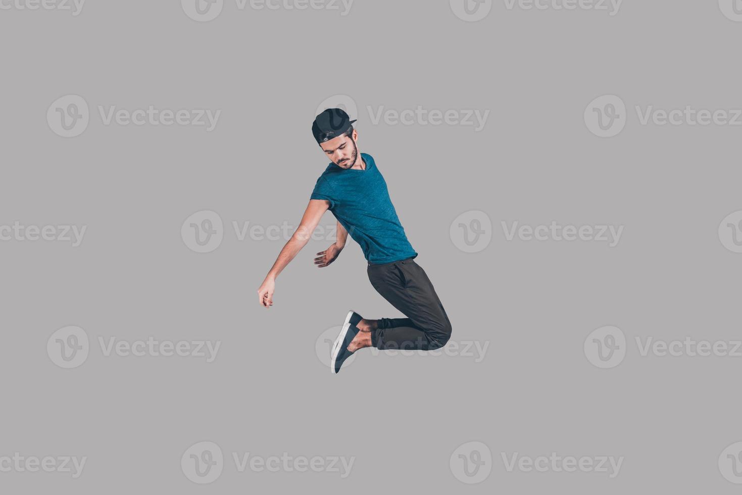 zorgeloos springen. in de lucht schot van knap jong Mens in pet jumping en gebaren tegen achtergrond foto