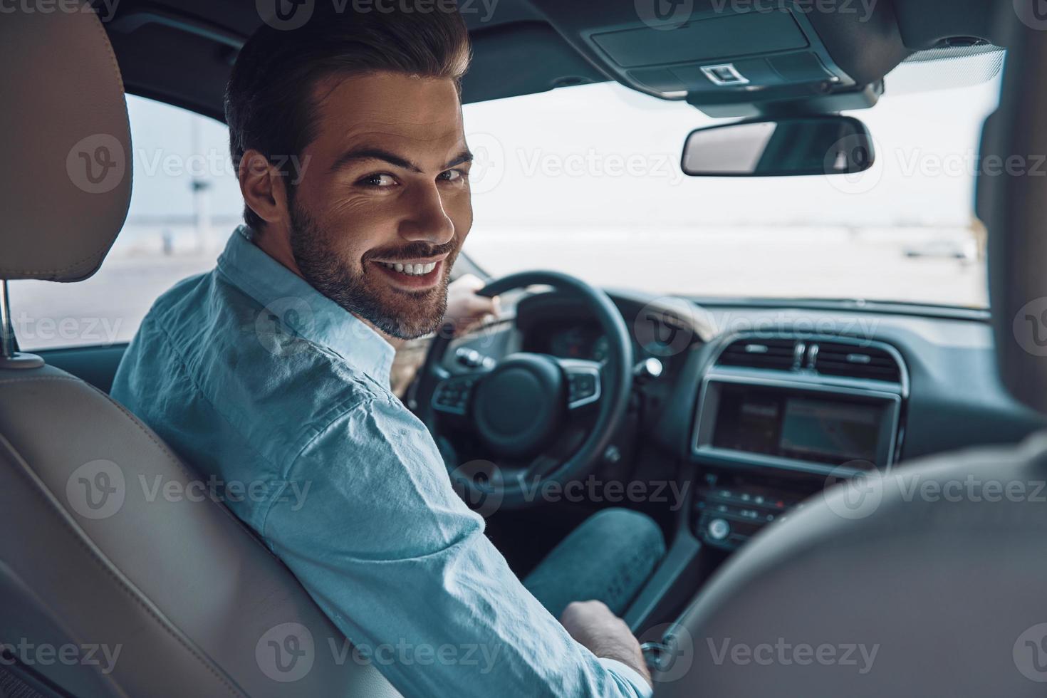 zijn u klaar naar g achterzijde visie van jong Mens in slim gewoontjes slijtage op zoek Bij camera over- schouder en glimlachen terwijl het rijden een toestand auto foto