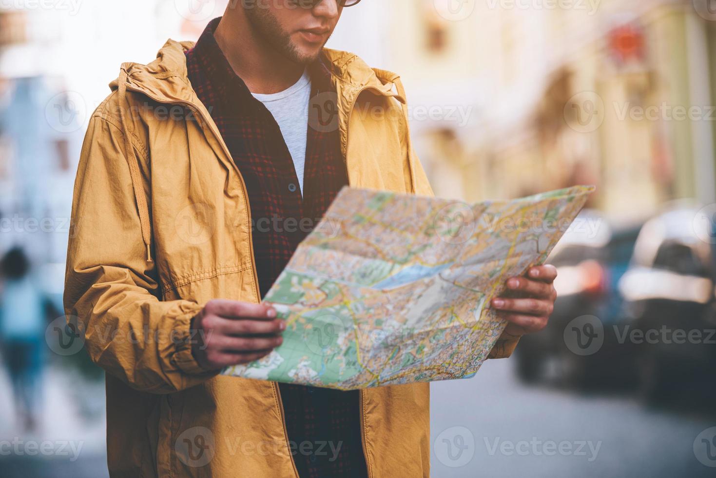 ontdekken nieuw plaatsen. detailopname van knap jong Mens Holding kaart en op zoek Bij het terwijl staand Aan de stad straat foto