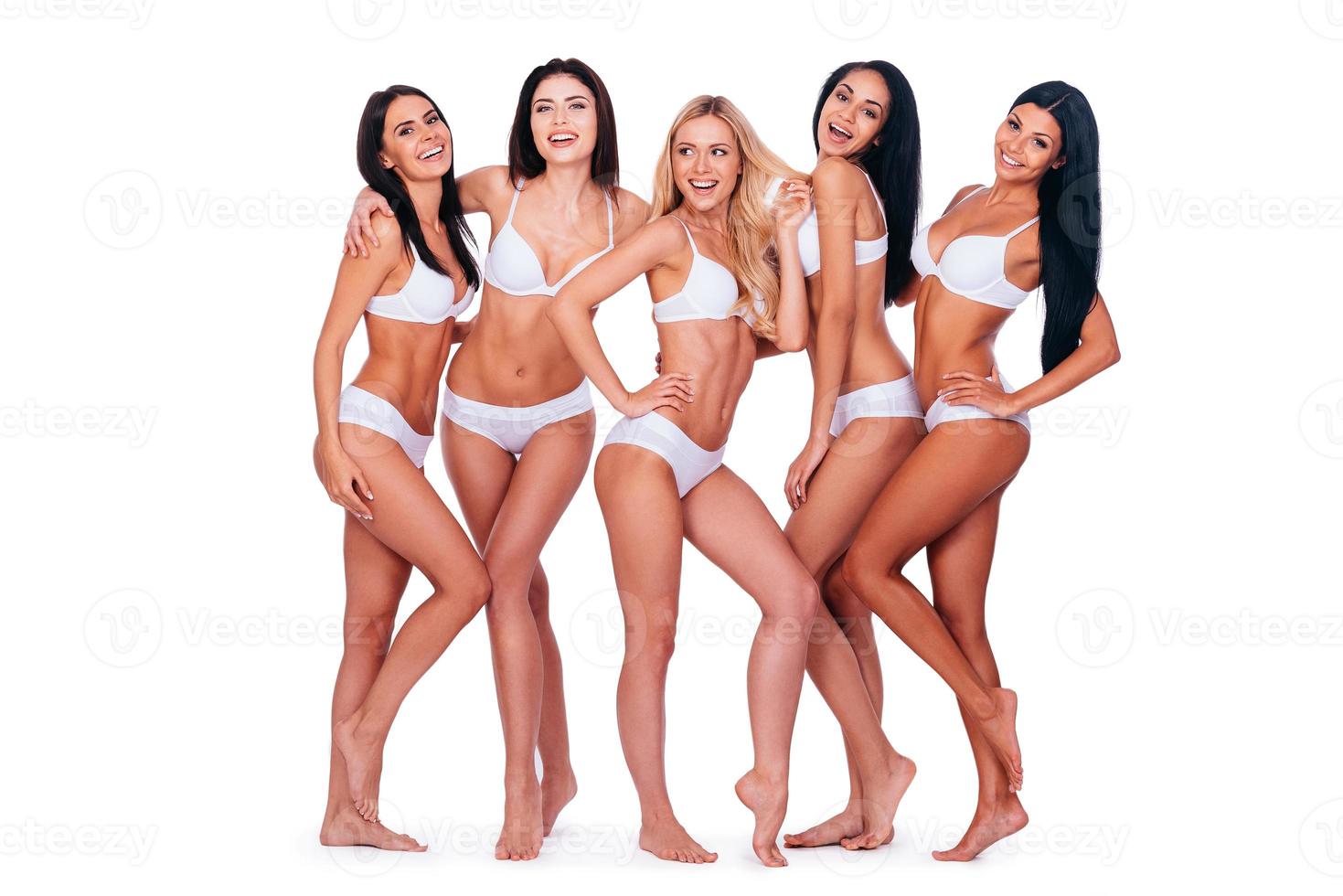 natuurlijk schoonheid. vol lengte van vijf mooi jong Dames in lingerie poseren en glimlachen terwijl bonding naar elk andere en staand tegen wit achtergrond foto