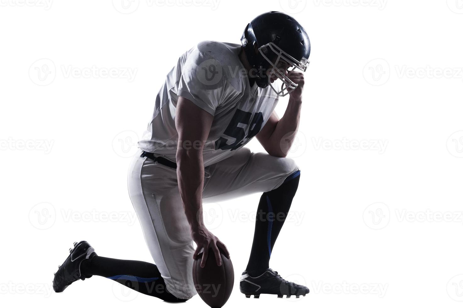 voorbereidingen treffen naar groot spel. kant visie van Amerikaans Amerikaans voetbal speler Holding hand- Aan helm terwijl staand Aan knie tegen wit achtergrond foto