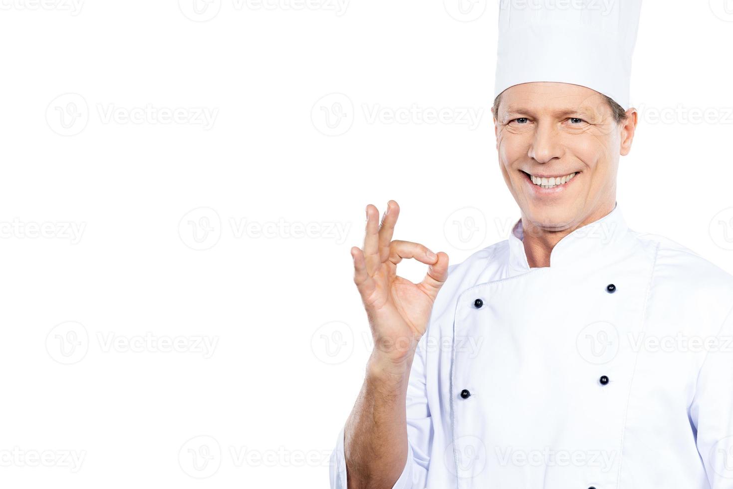 meester chef. zelfverzekerd volwassen chef in wit uniform gebaren OK teken en glimlachen terwijl staand tegen wit achtergrond foto