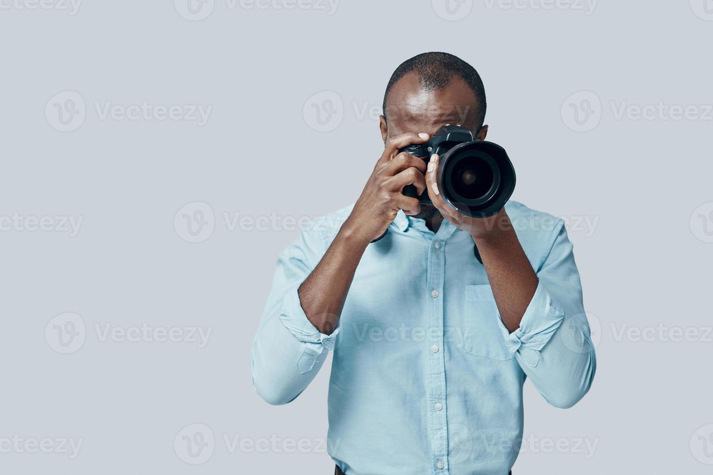 charmant jong Afrikaanse Mens nemen een foto gebruik makend van digitaal camera terwijl staand tegen grijs achtergrond