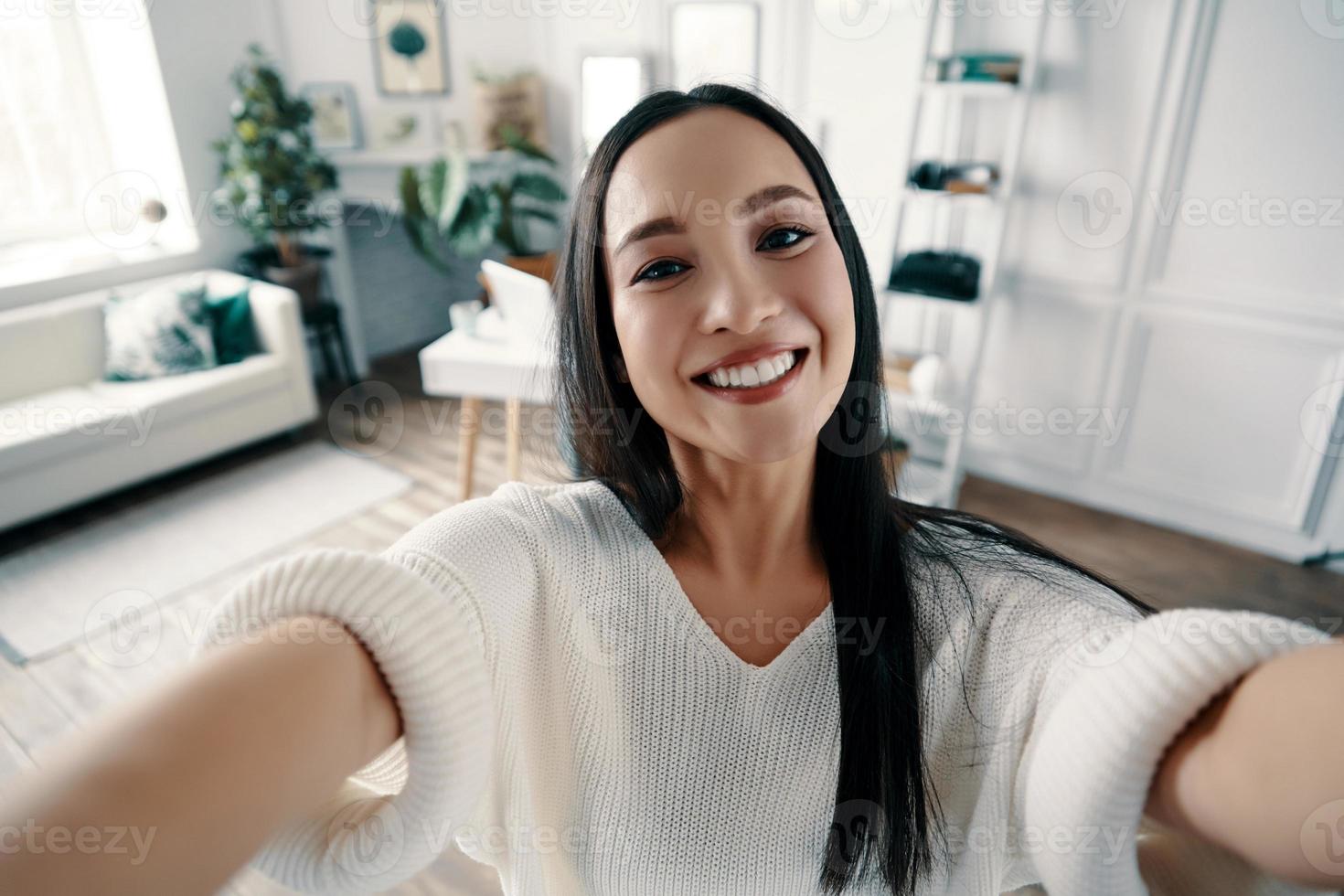 perfect selfie. aantrekkelijk jong vrouw op zoek Bij camera en glimlachen terwijl nemen selfie Bij huis foto