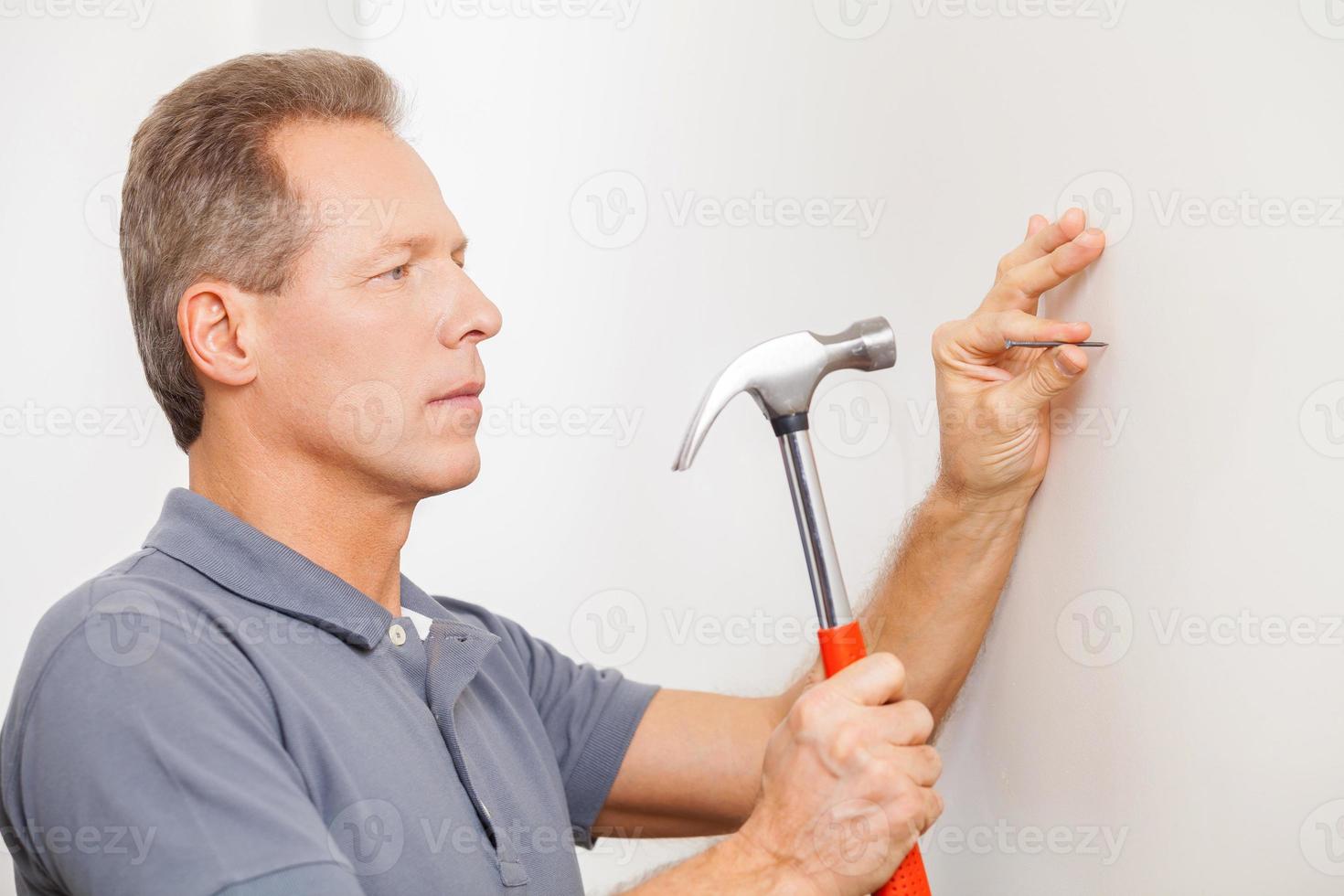 Mens hameren een nagel. zelfverzekerd volwassen grijs haar- Mens hameren een nagel foto