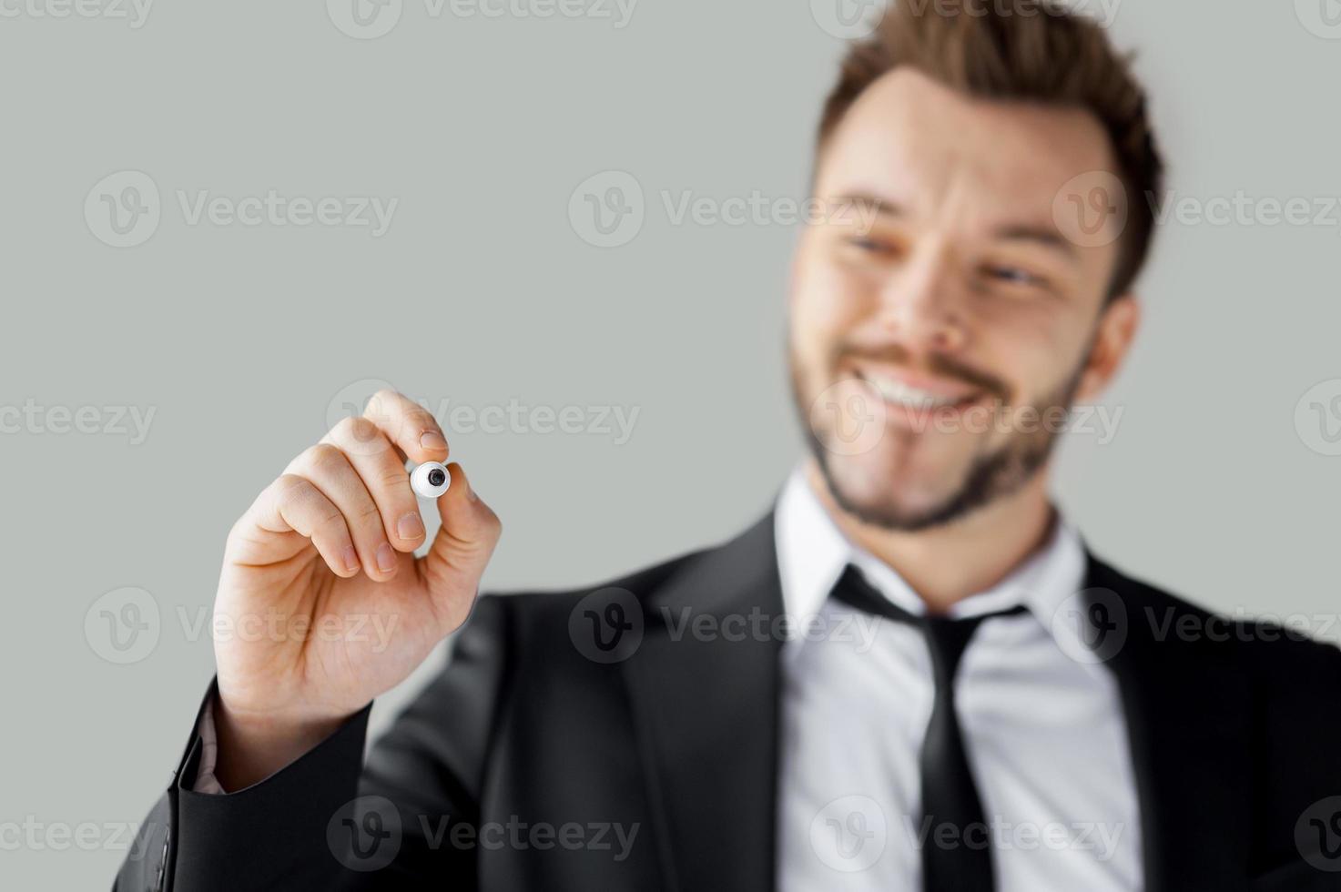 zakenman schrijven op transparante wandbord. vrolijke jonge man in formalwear schrijven iets op transparante veeg boord terwijl je tegen een grijze achtergrond foto