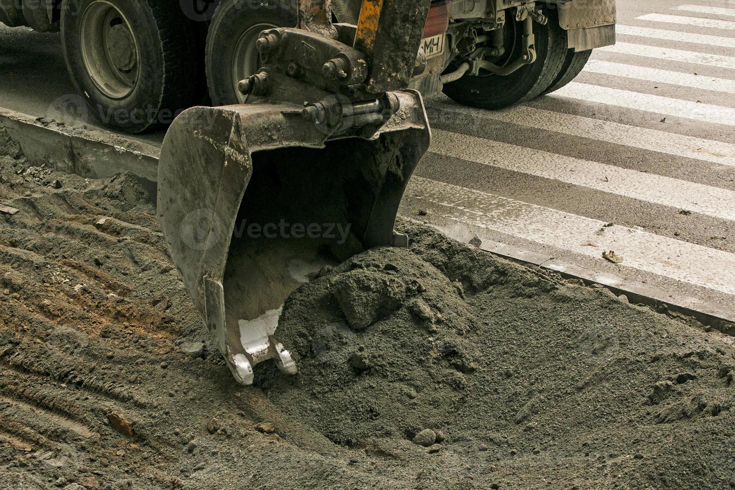 weg werken Aan de stad straat. de graafmachine emmer verzamelt de oud bestrating en ladingen het in een dump vrachtauto foto