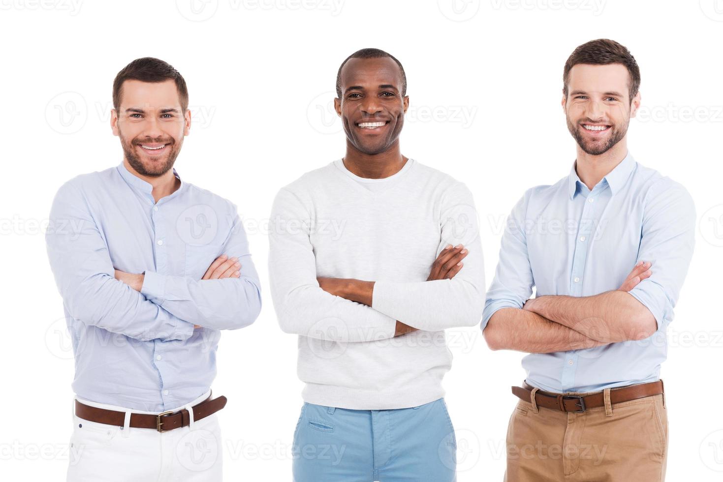 jong en succesvol. drie zelfverzekerd jong mannen in slim gewoontjes slijtage houden armen gekruiste en glimlachen terwijl staand tegen wit achtergrond foto