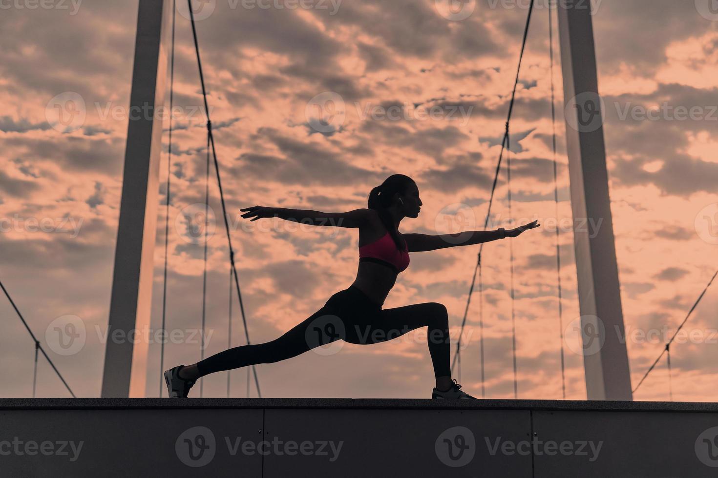 vind uw evenwicht. modern jong vrouw in sport- kleding uitrekken terwijl opwarming omhoog buitenshuis foto