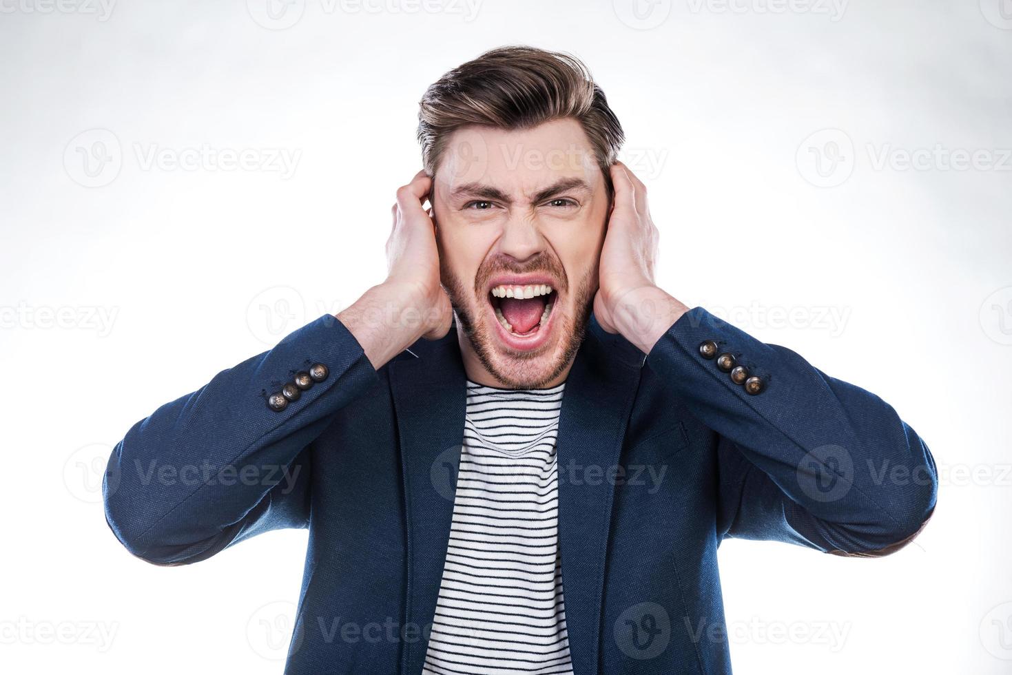 benadrukt Mens. portret van woedend jong Mens grimassen en aan het bedekken oren met handen terwijl staand tegen wit achtergrond foto