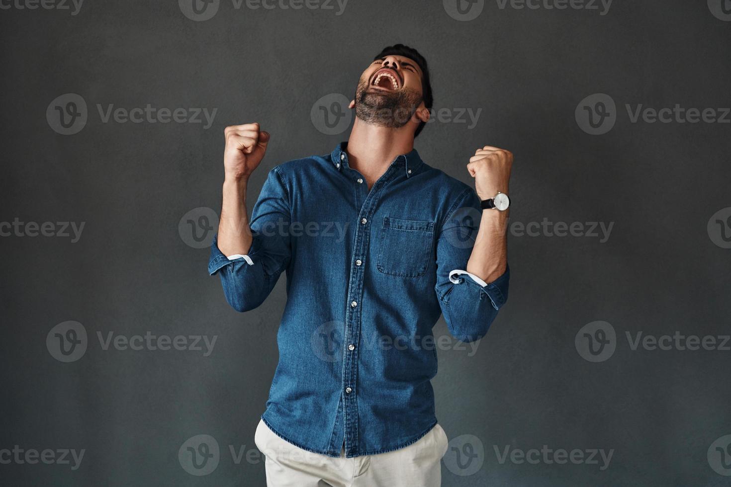 knap jong Mens in denim overhemd gebaren terwijl staand tegen grijs achtergrond foto