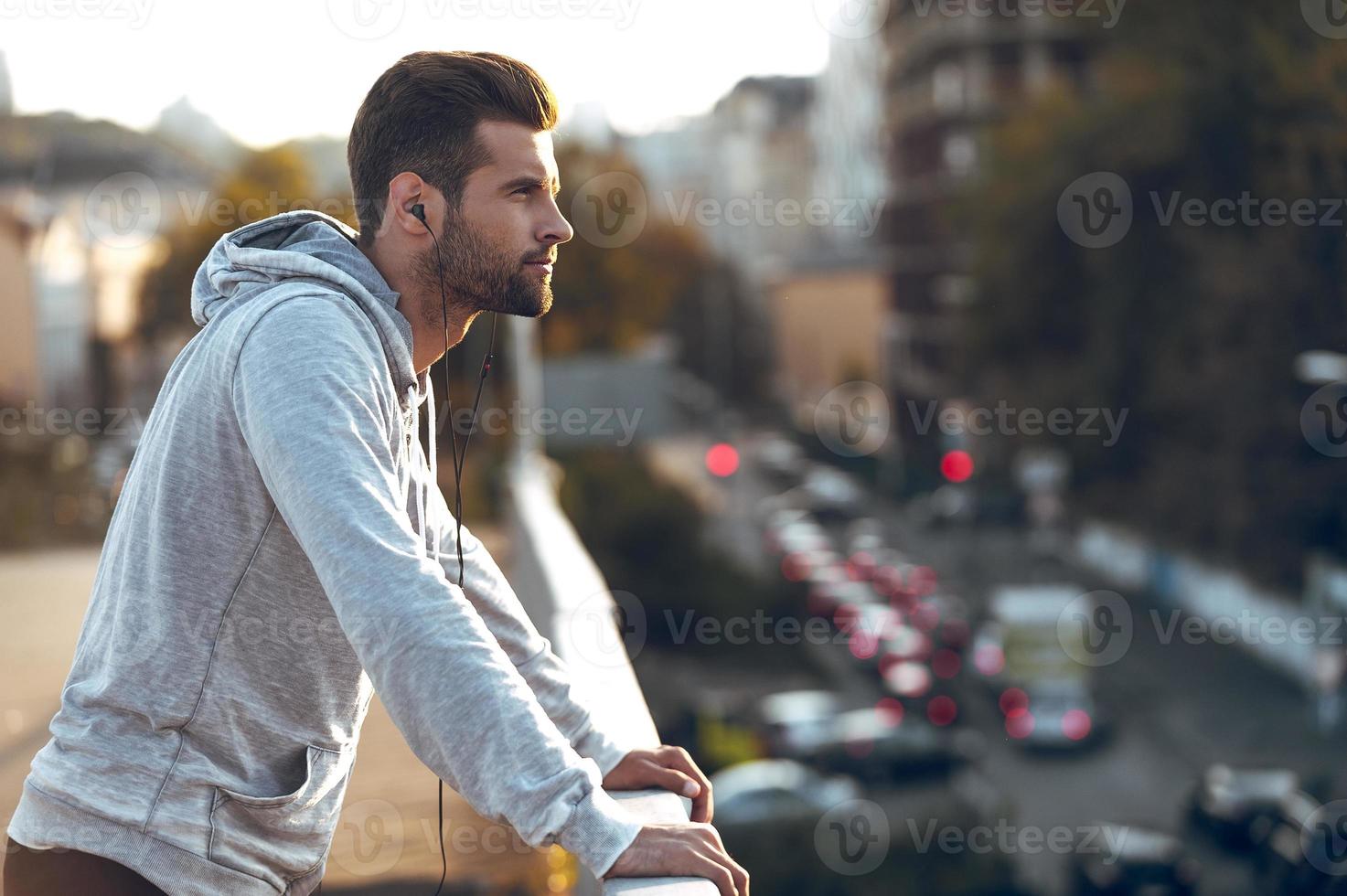 in liefde met zijn stad. kant visie van nadenkend jong Mens in hoofdtelefoons op zoek weg terwijl staand Aan de brug foto