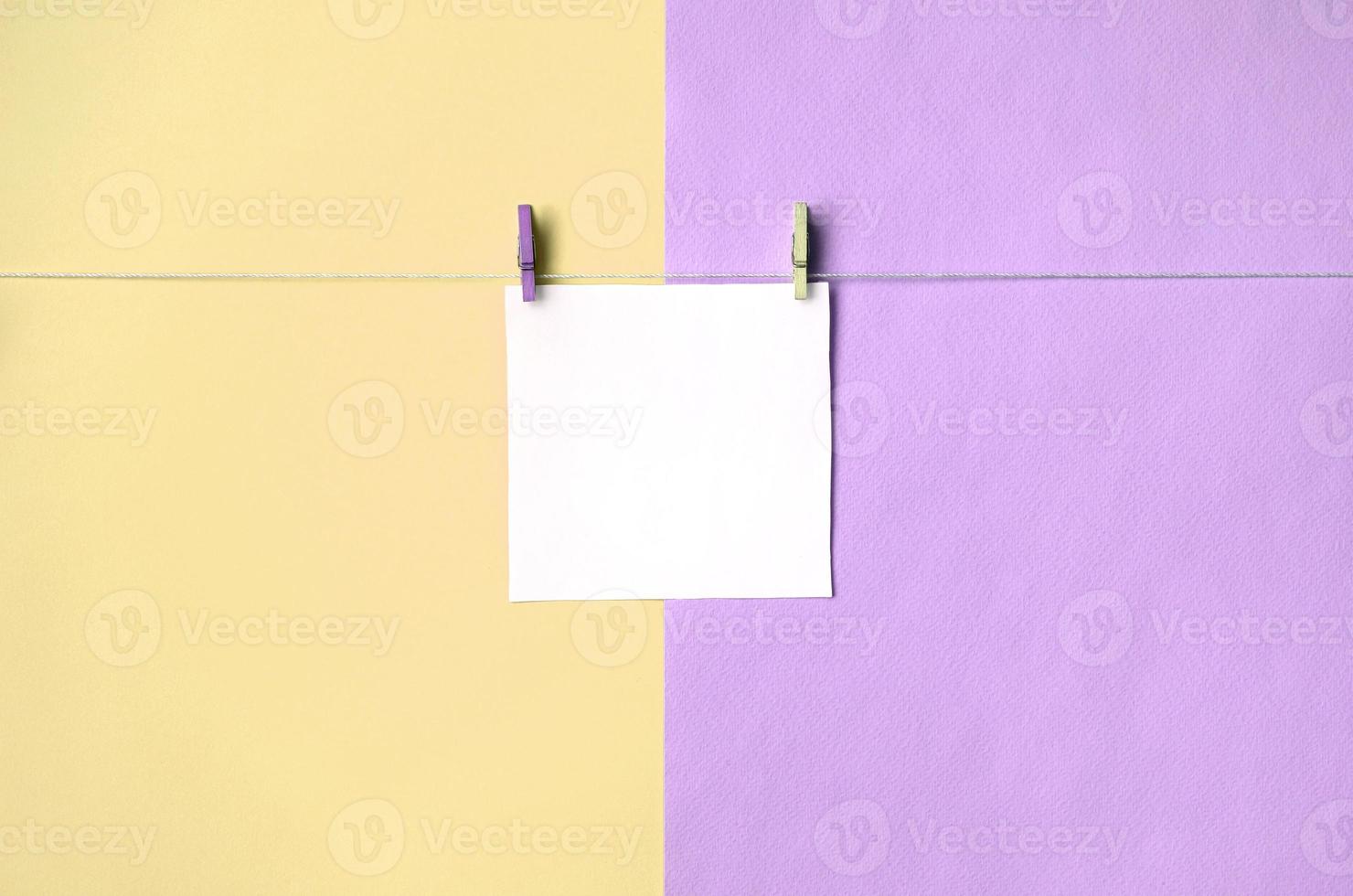 een stuk van papier is hangende Aan een touw met haringen Aan structuur achtergrond van mode pastel geel en paars kleuren foto