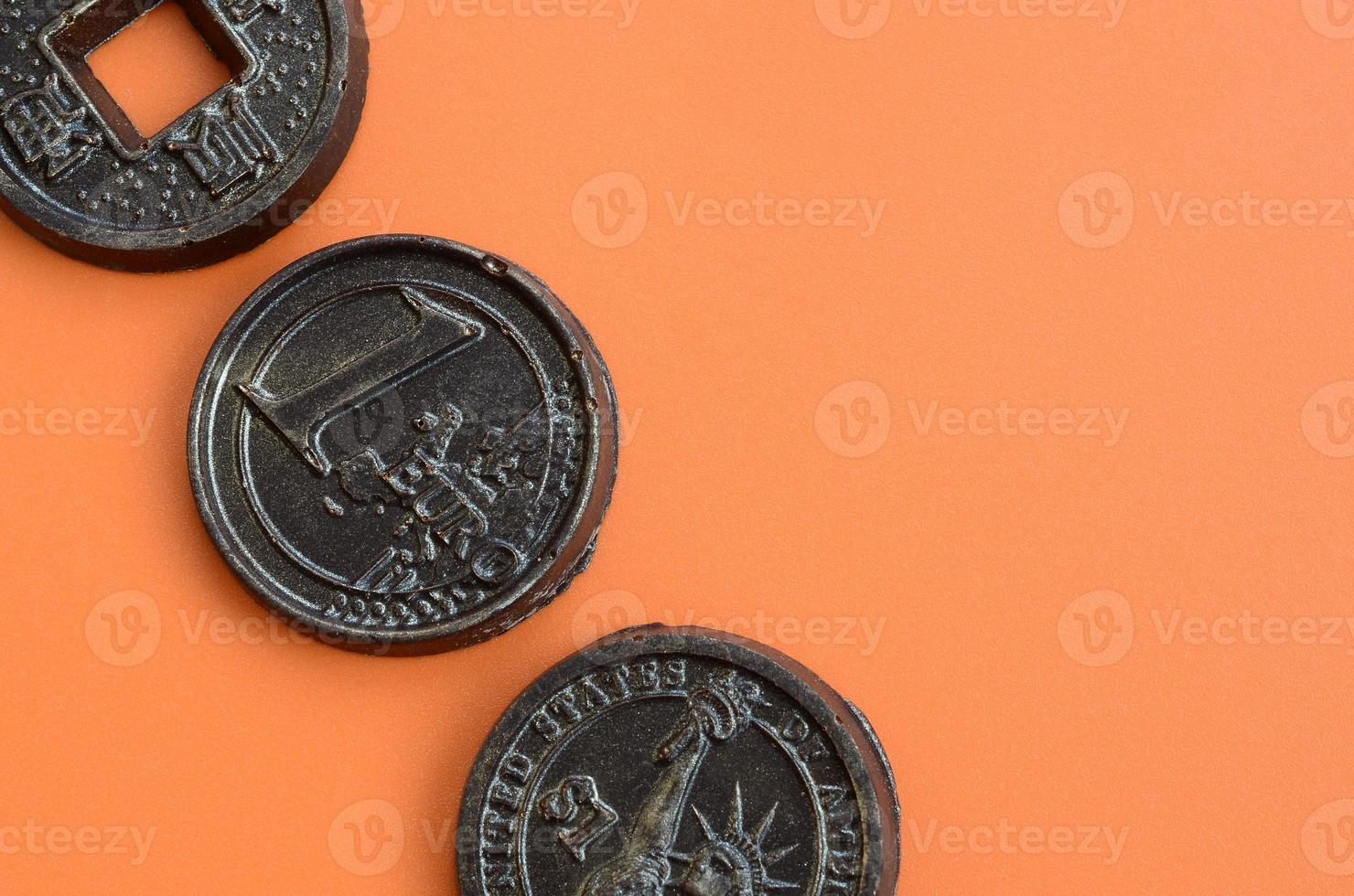 drie chocola producten in de het formulier van euro, Verenigde Staten van Amerika en Japan munten liggen Aan een oranje plastic achtergrond. een model- van contant geld munten in een eetbaar het formulier foto