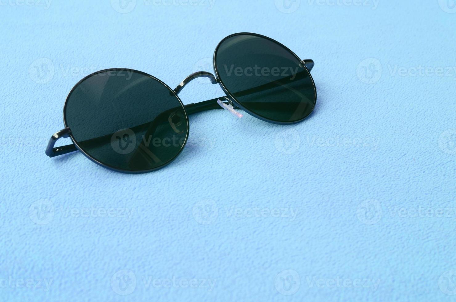 elegant zwart zonnebril met ronde bril leugens Aan een deken gemaakt van zacht en pluizig licht blauw fleece kleding stof. modieus achtergrond afbeelding in vrouw kleuren foto