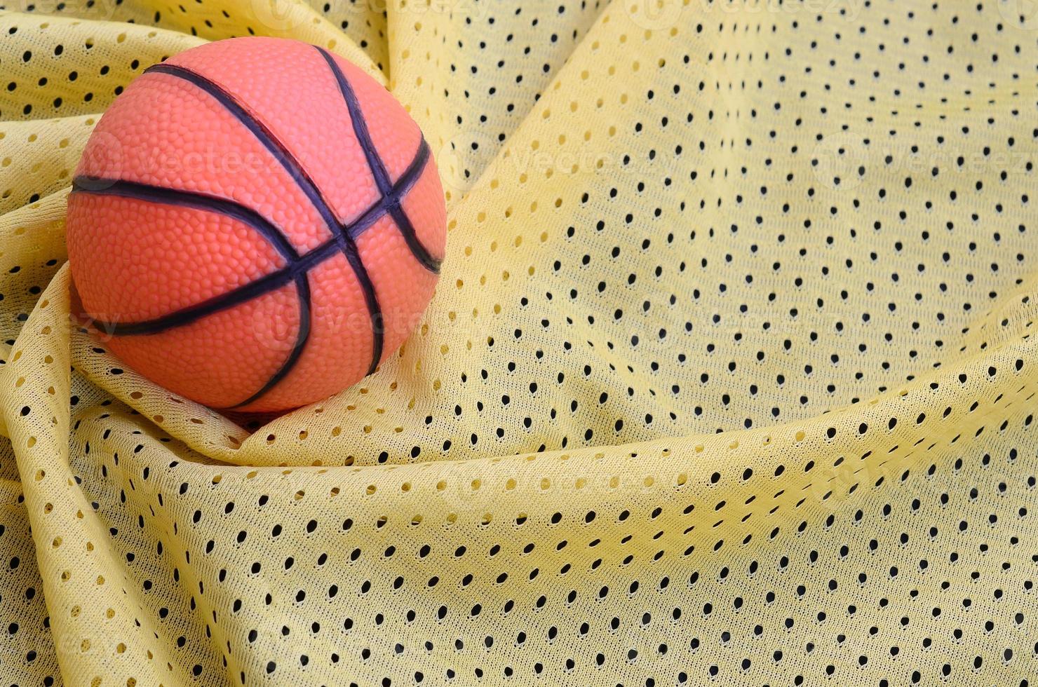 klein oranje rubber basketbal leugens Aan een geel sport Jersey kleding kleding stof structuur en achtergrond met veel vouwen foto