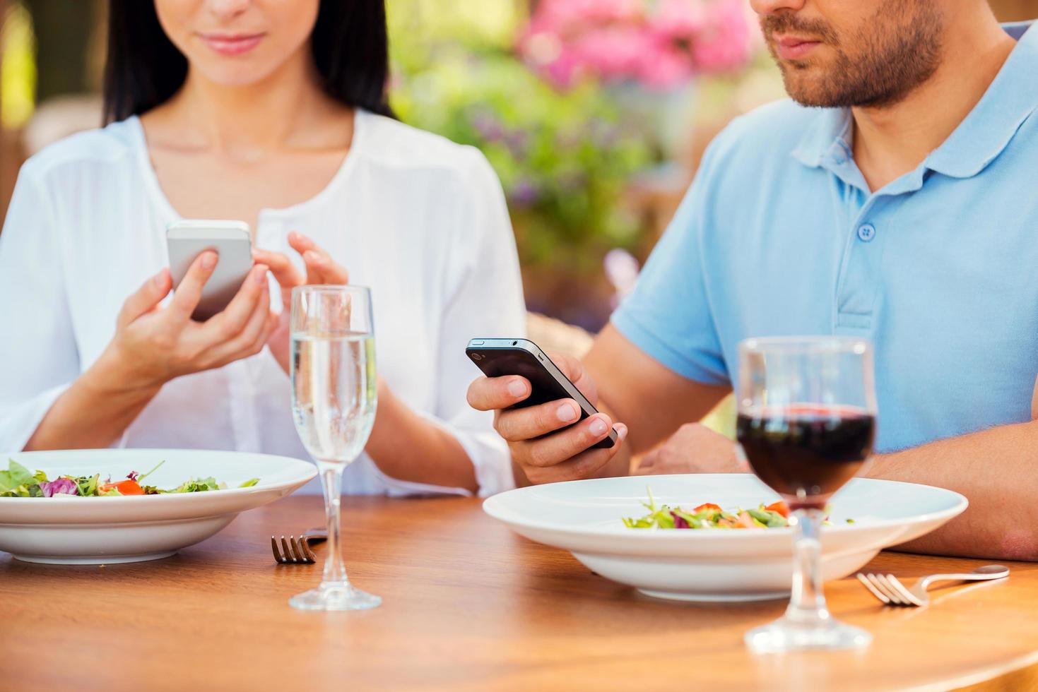 in hun scheiden s werelds. detailopname van jong paar typen iets Aan hun slim telefoons terwijl ontspannende in buitenshuis restaurant samen foto