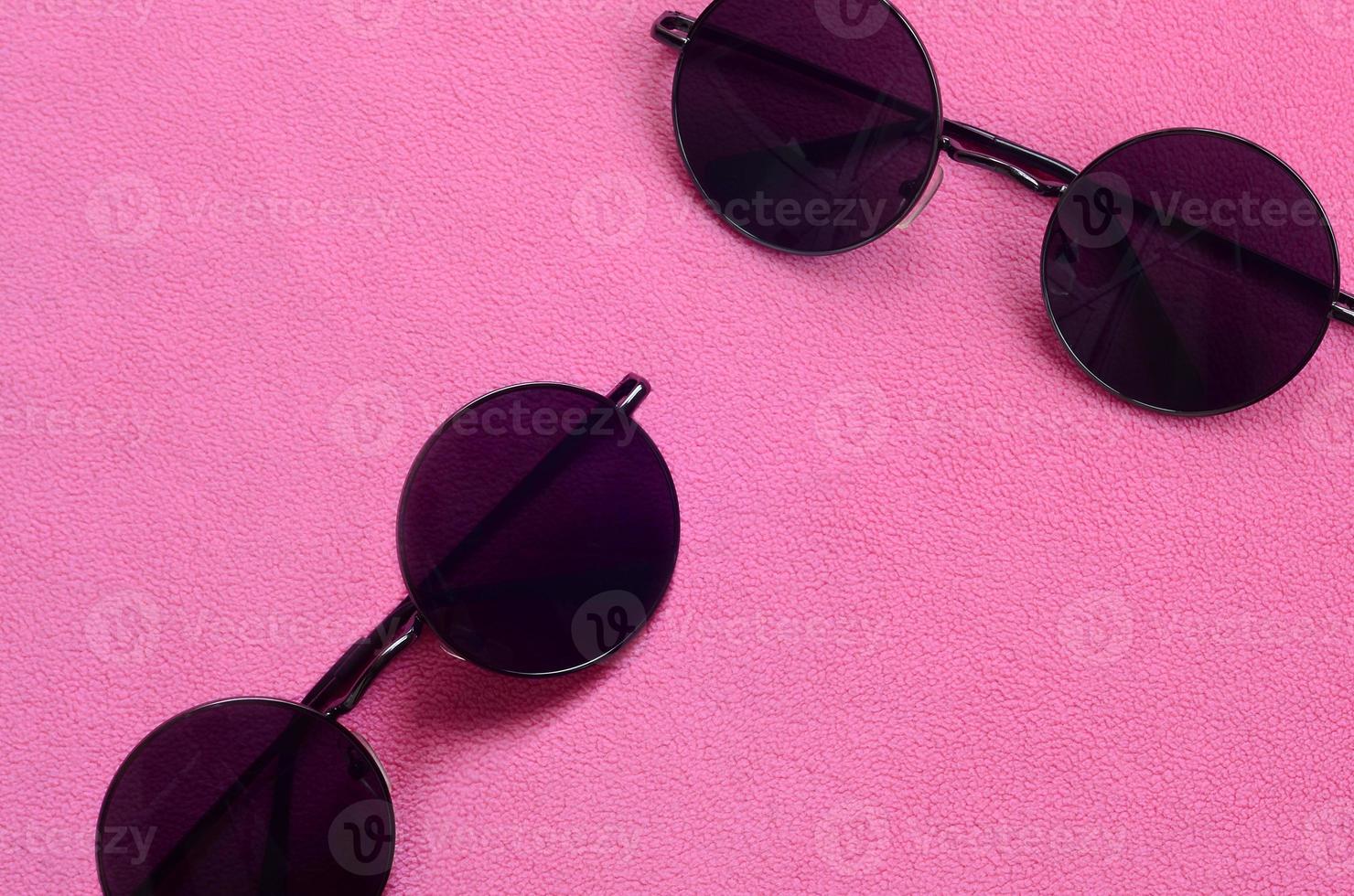 twee elegant zwart zonnebril met ronde bril leugens Aan een deken gemaakt van zacht en pluizig licht roze fleece kleding stof. modieus achtergrond afbeelding in vrouw kleuren foto