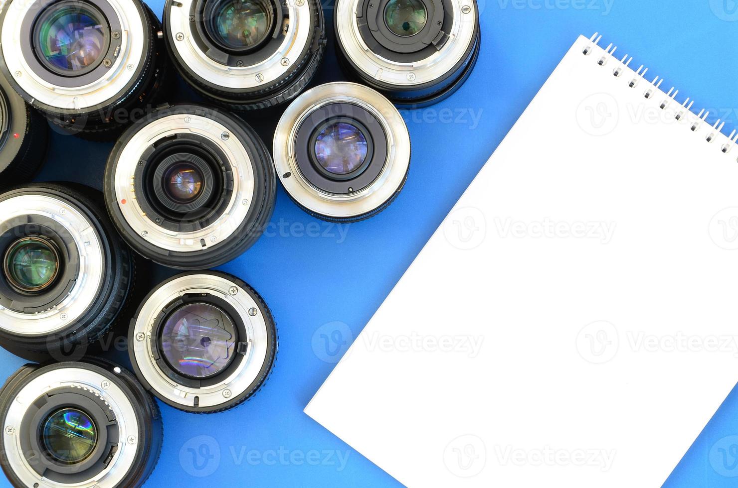 meerdere fotografisch lenzen en wit notitieboekje liggen Aan een helder blauw achtergrond. ruimte voor tekst foto