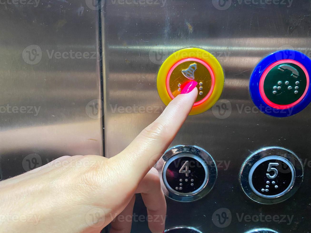 een vrouw gemanicuurd vinger Aan haar hand- persen een knop in een modern mooi lift in een hoogbouw gebouw foto